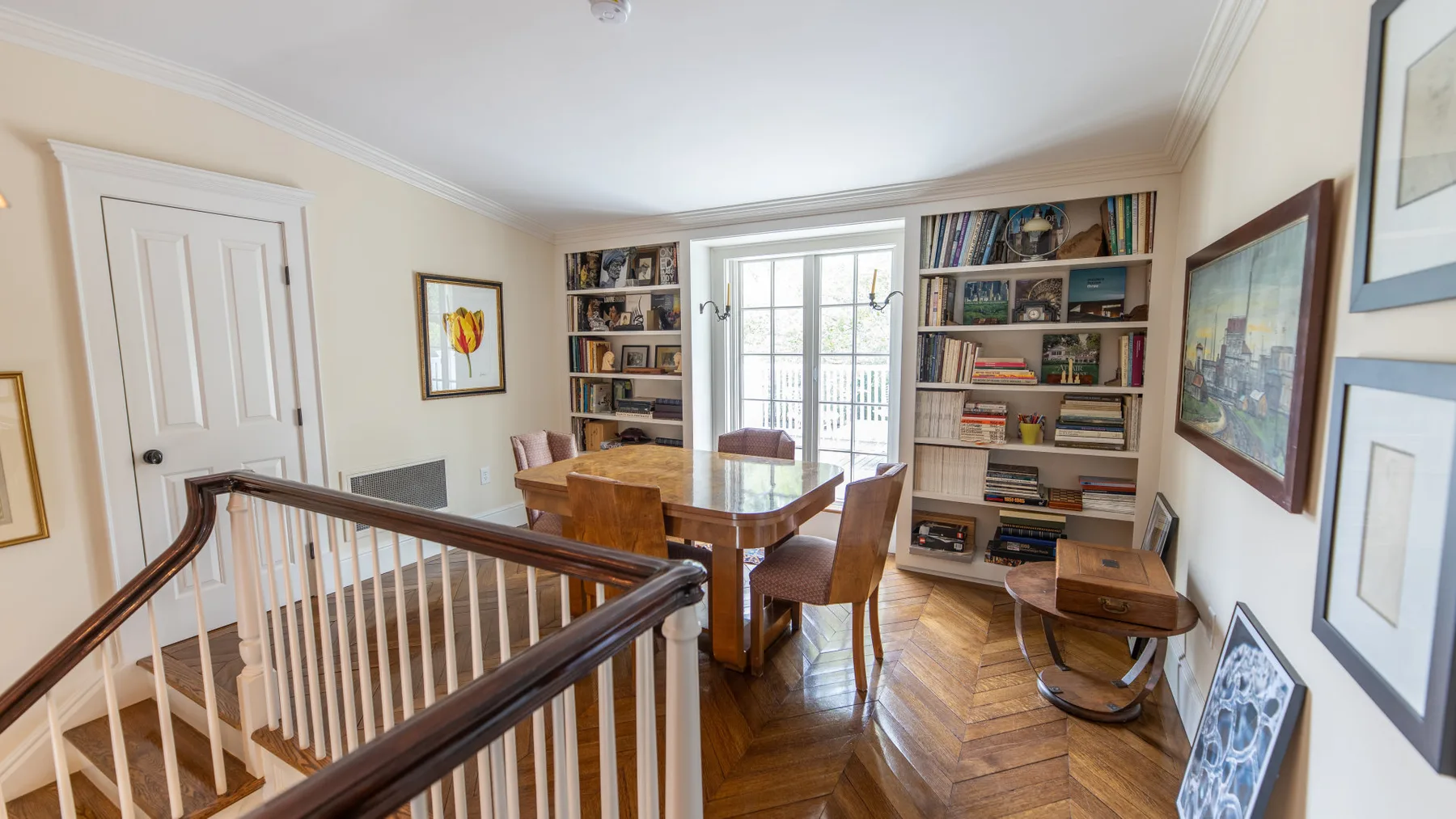 Un estudio luminoso con estanterías, una mesa de madera y sillas junto a las ventanas.