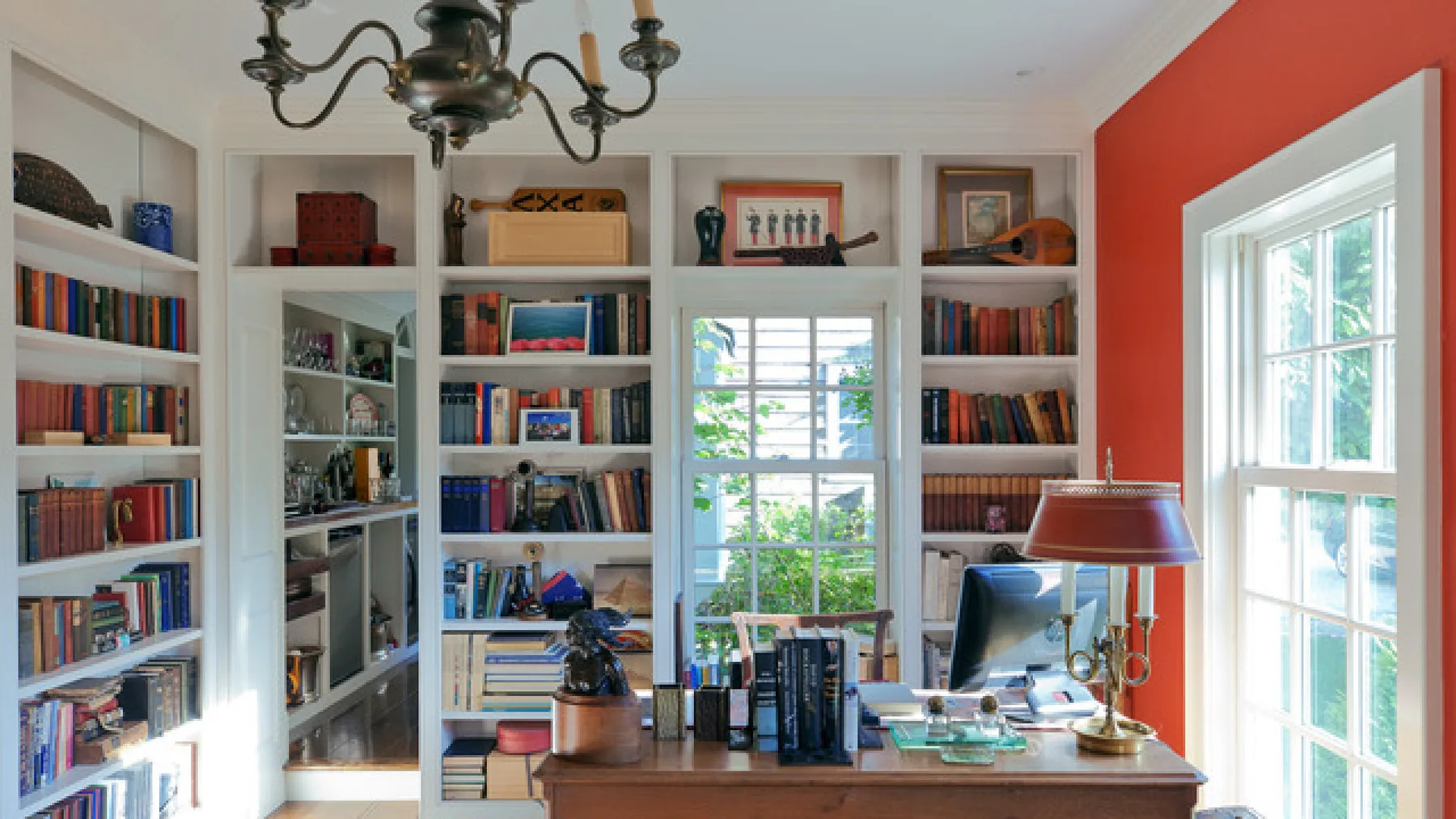 Una biblioteca en casa con estanterías empotradas, un escritorio y ventanas grandes.