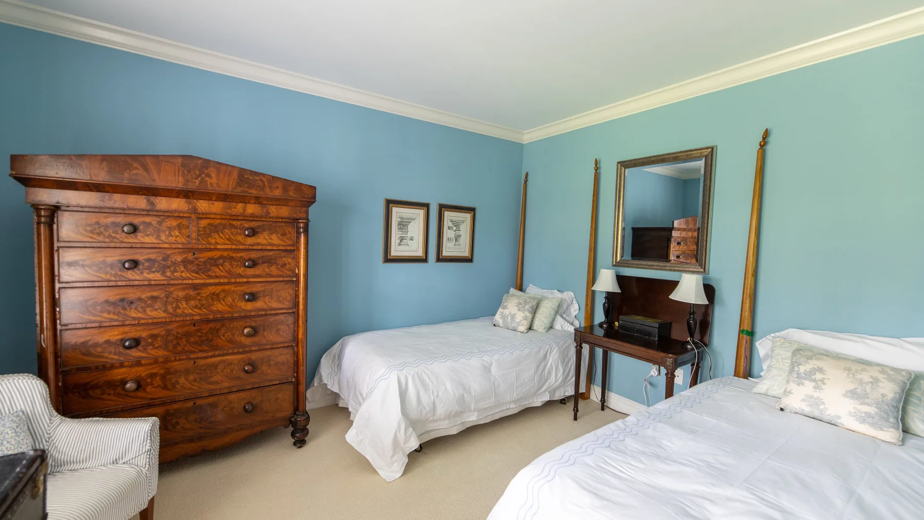 Un dormitorio azul con dos camas y una cómoda de madera.