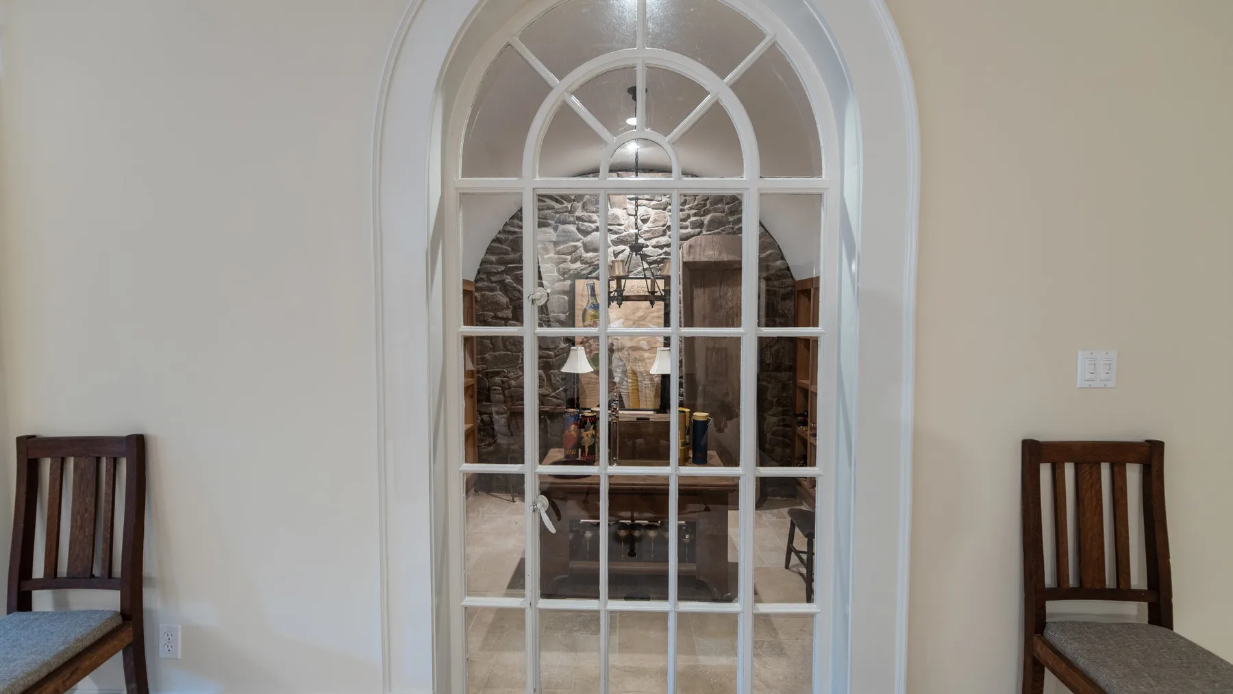Una división acristalada en arco deja ver un comedor con mesa y sillas.
