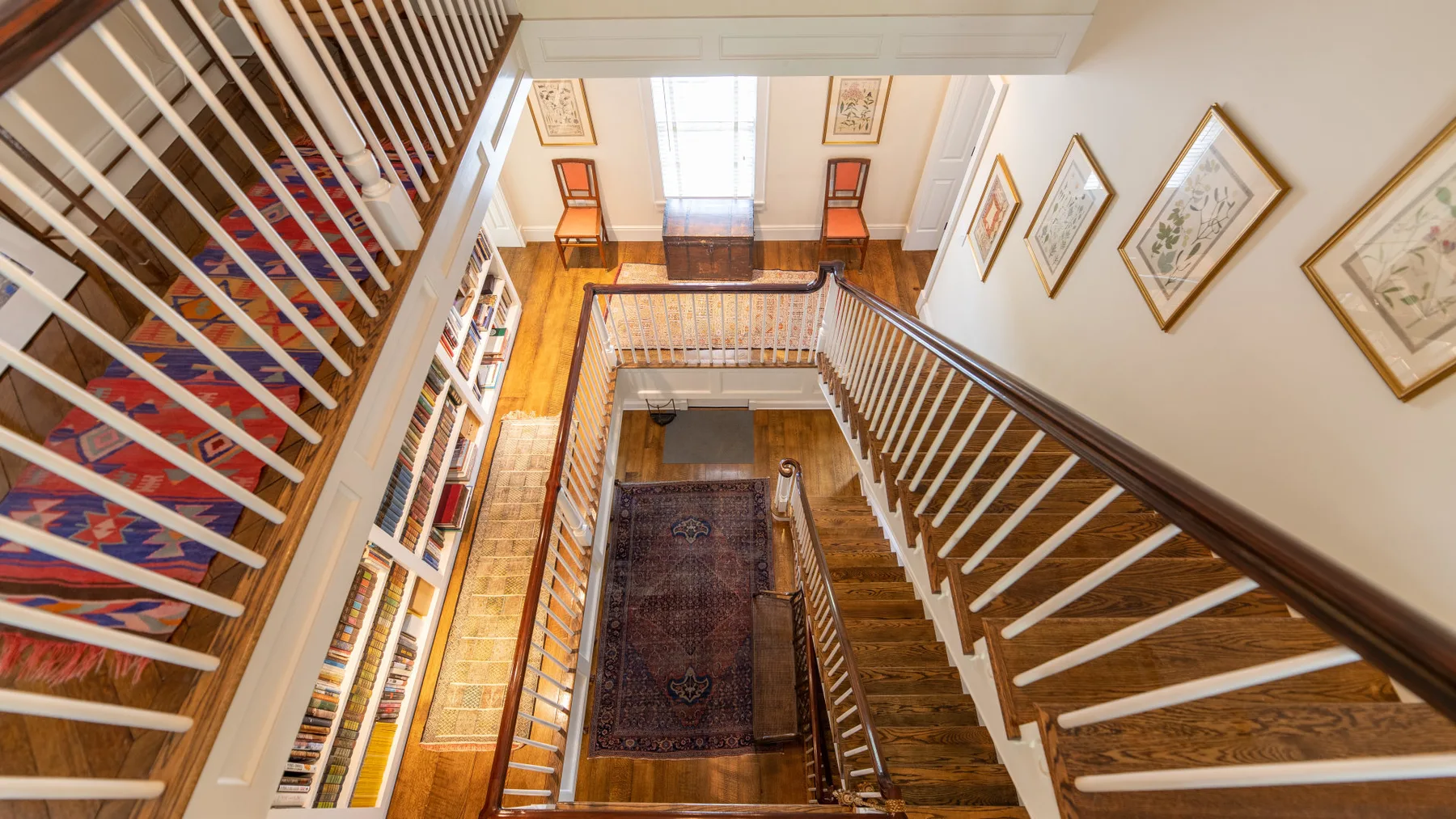 Una escalera con peldaños de madera, barandillas blancas y cuadros en las paredes.