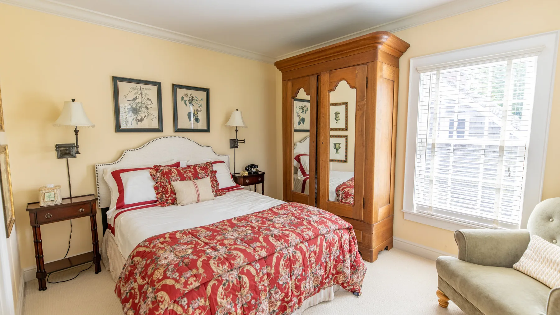 Un dormitorio con una cama cubierta con una colcha floral roja y un armario de madera.