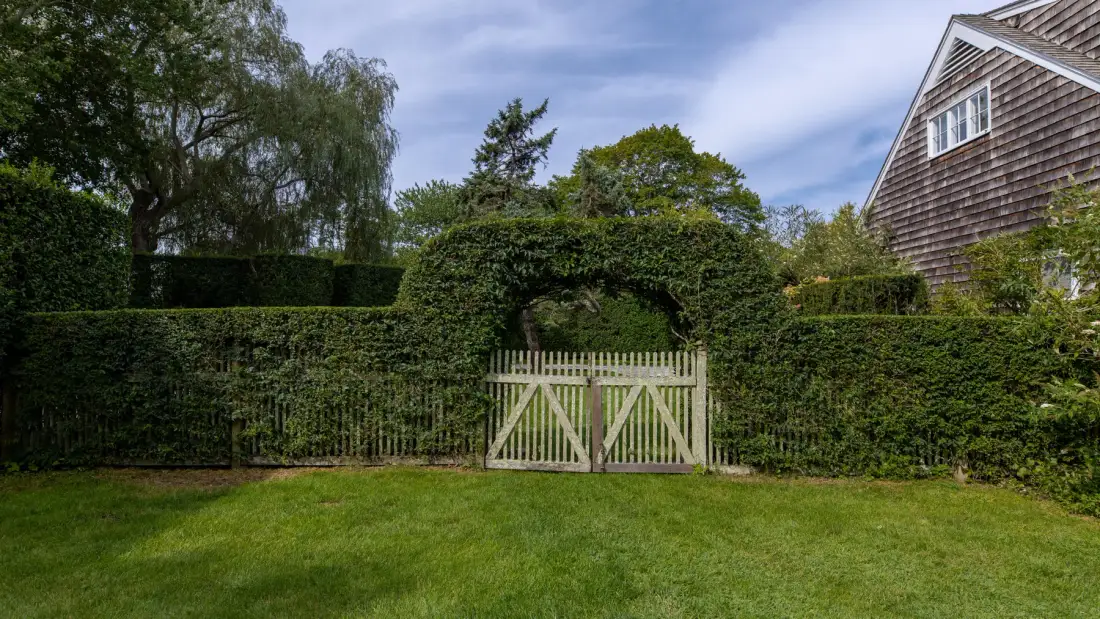Un jardín de césped conduce a una puerta de madera en un seto alto.