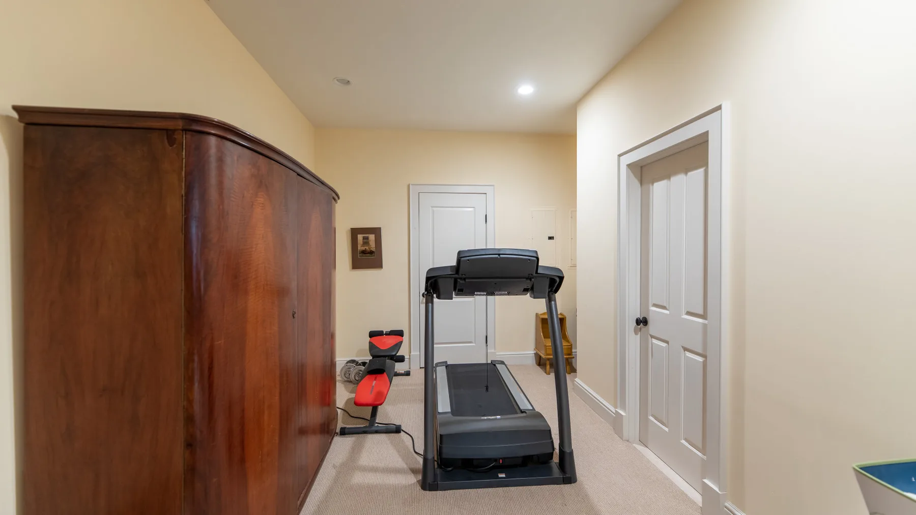 Habitación con alfombra beige, una caminadora y un armario grande de madera.
