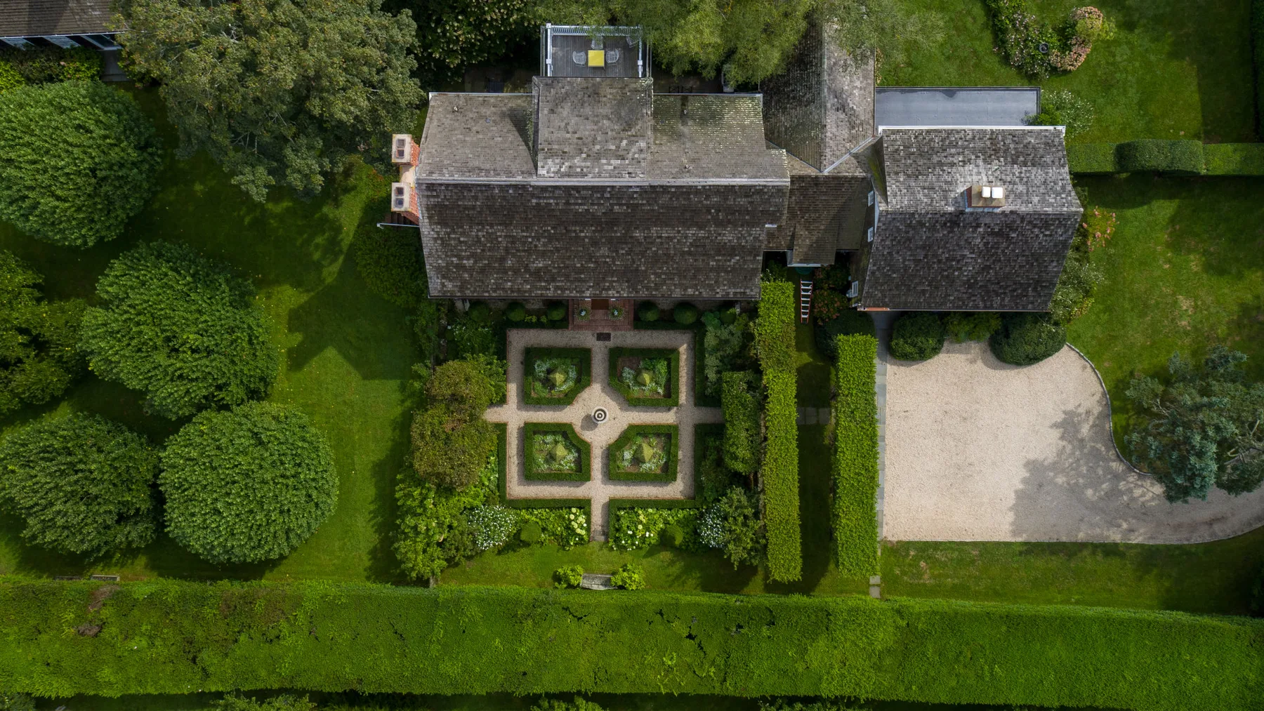 Vista aérea de una casa junto a un jardín formal y un patio pavimentado.