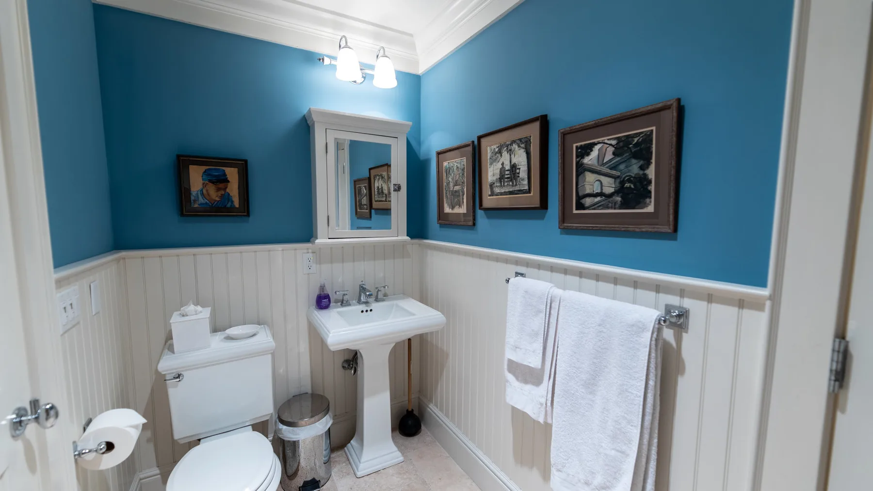Un baño azul con lavabo de pedestal, espejo de pared y cuadros enmarcados.