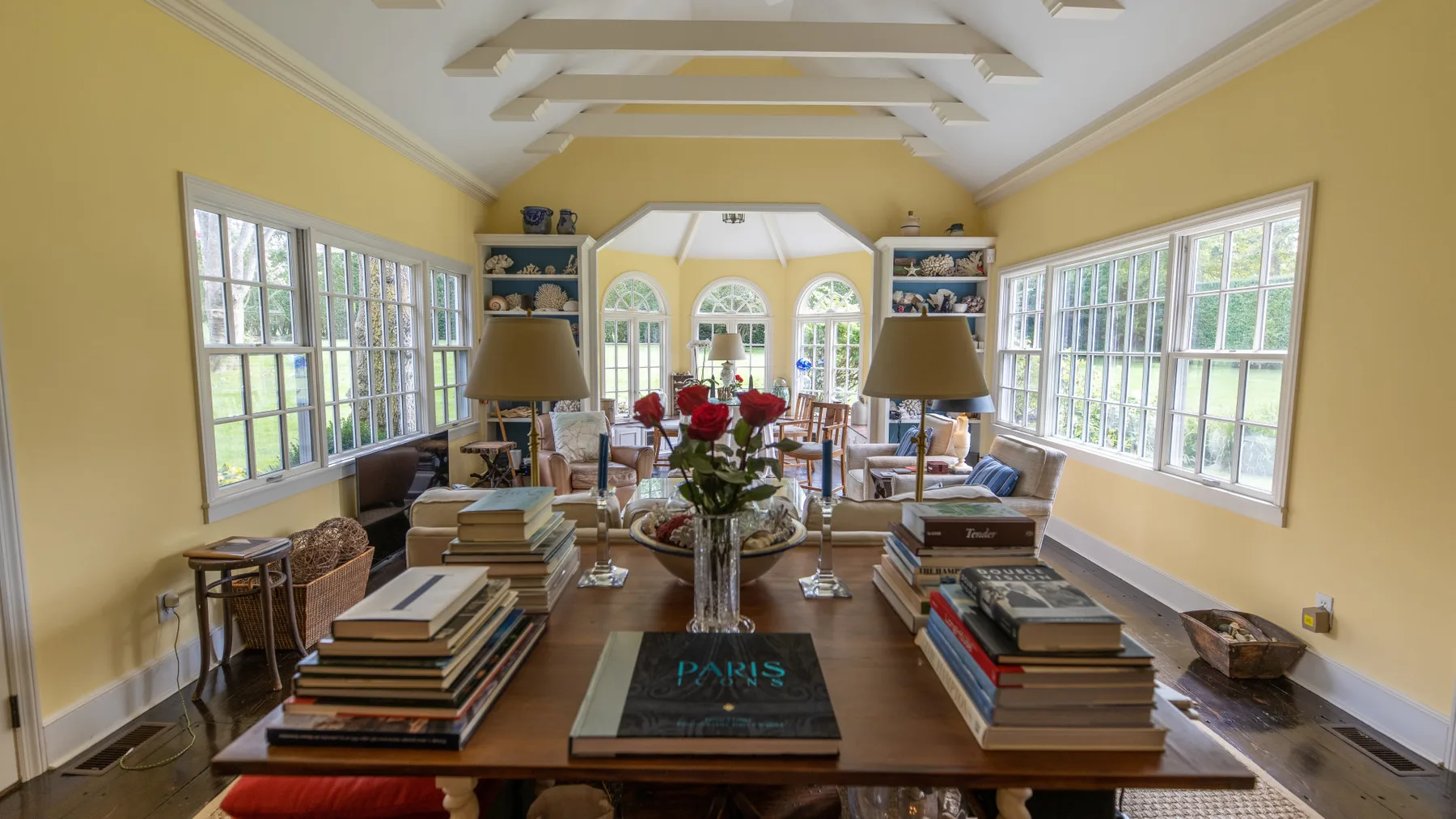 Un solárium luminoso con mesas largas, libros y grandes ventanas.