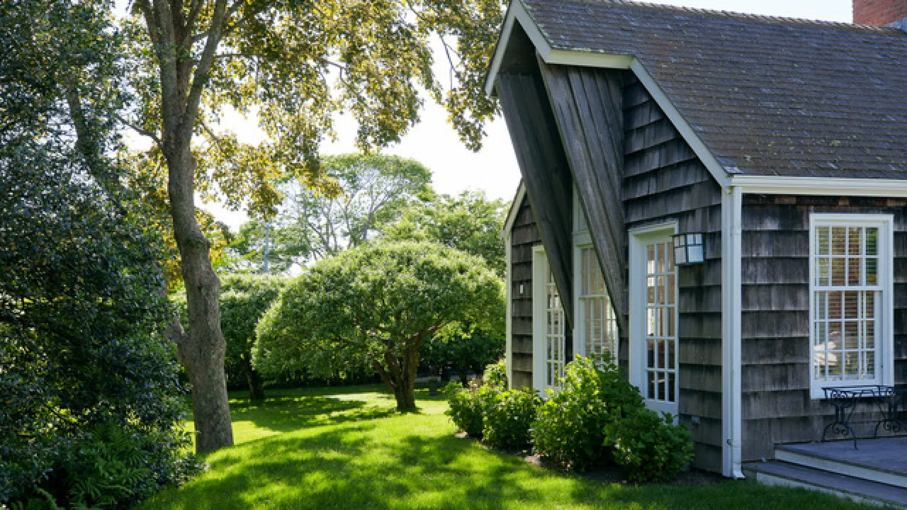 Una casa de fachada oscura está junto a un césped verde y árboles frondosos.