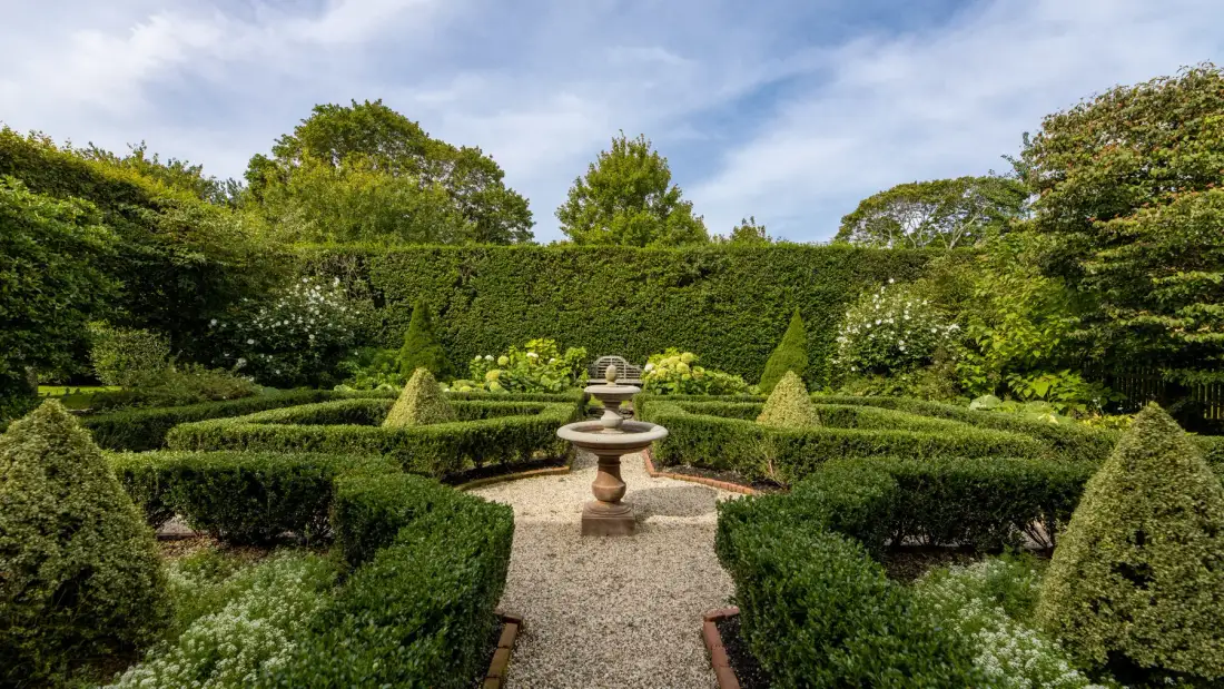 Un jardín formal con setos recortados y una fuente de piedra central.