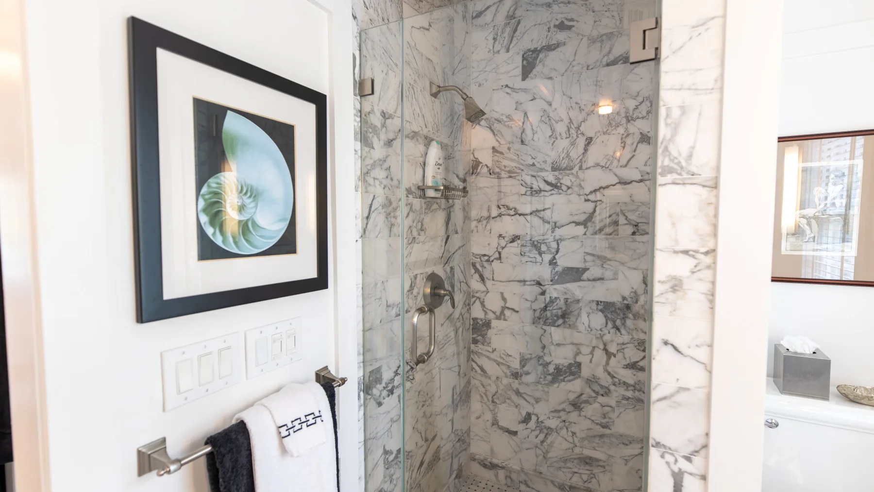 Una ducha de baño con azulejos de mármol, arte enmarcado y toallas cerca.