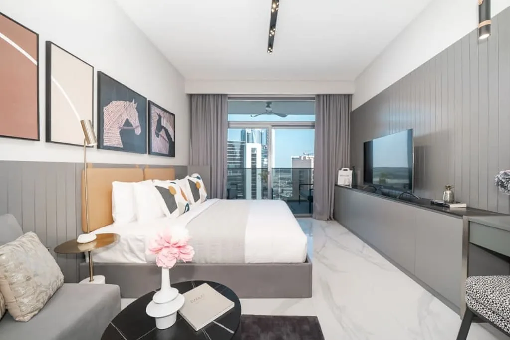 Un dormitorio moderno con una cama frente a un televisor y puertas de vidrio.