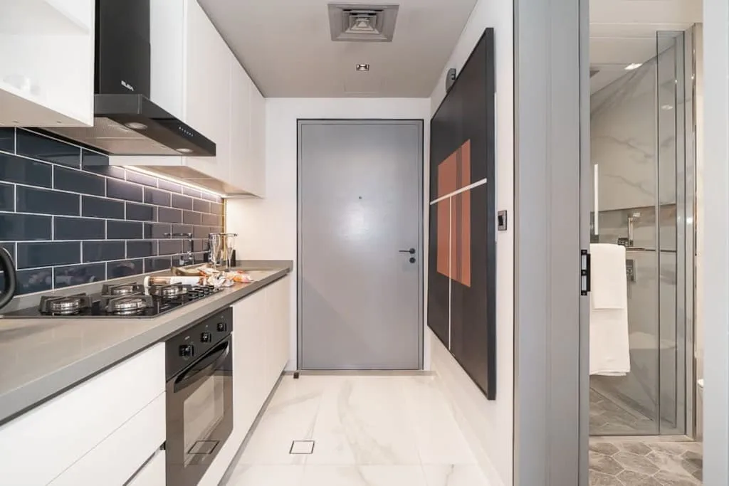 Una cocina compacta con salpicadero de azulejos oscuros y una puerta gris al fondo.