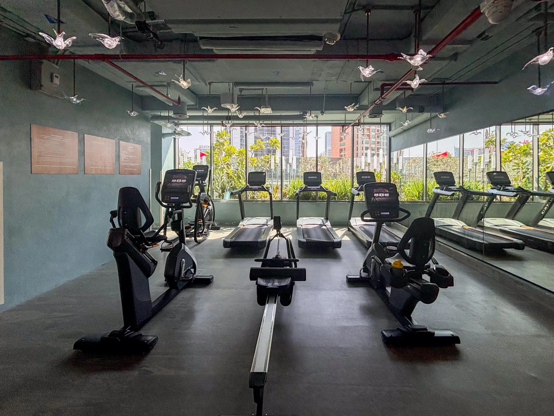 Un gimnasio con bicicletas estáticas, cintas de correr y grandes ventanas con vistas a zonas verdes.