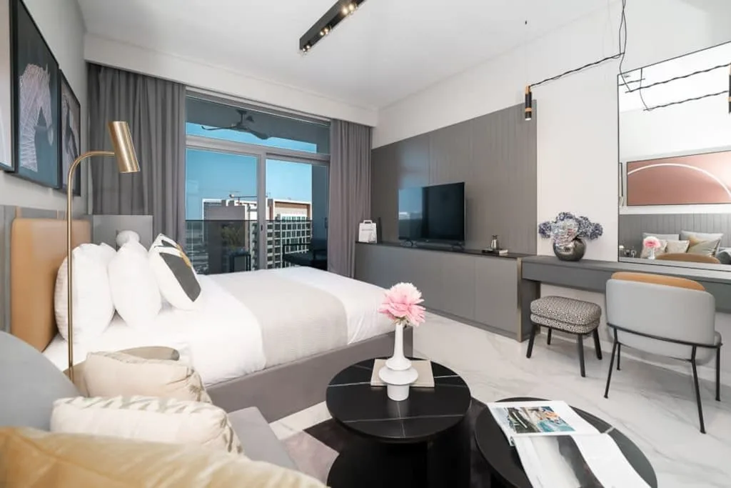 Un dormitorio moderno con cama, televisión y asientos junto a las ventanas.