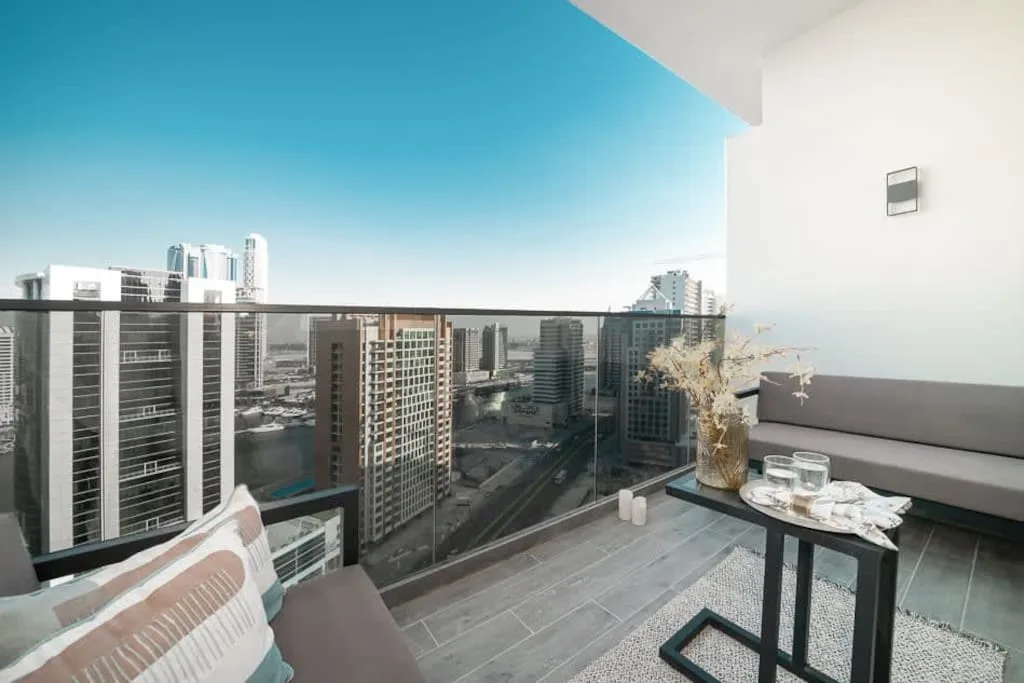 Una zona de estar en el balcón ofrece vistas de edificios altos bajo un cielo despejado.