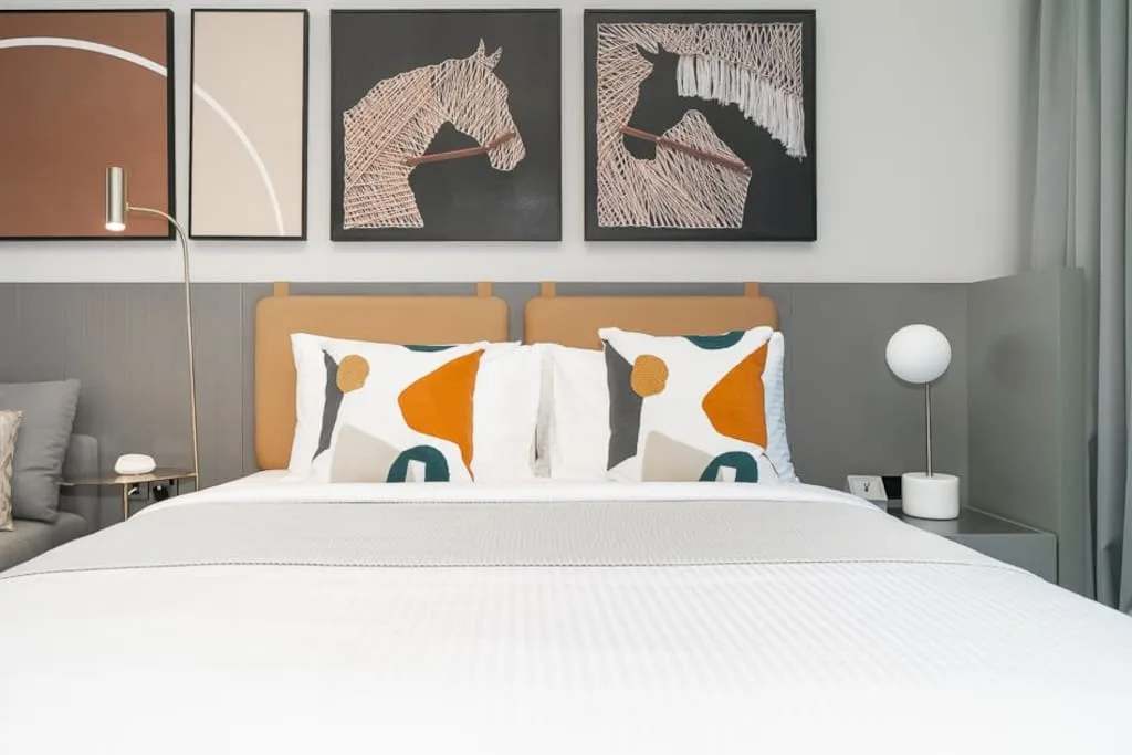 Un dormitorio con una cama tendida, cojines de colores y cuadros sobre el cabecero.