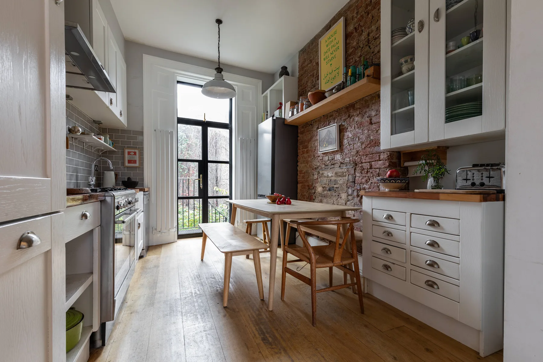 A bright kitchen with white cabinets, a wooden dining table, and a tall window.