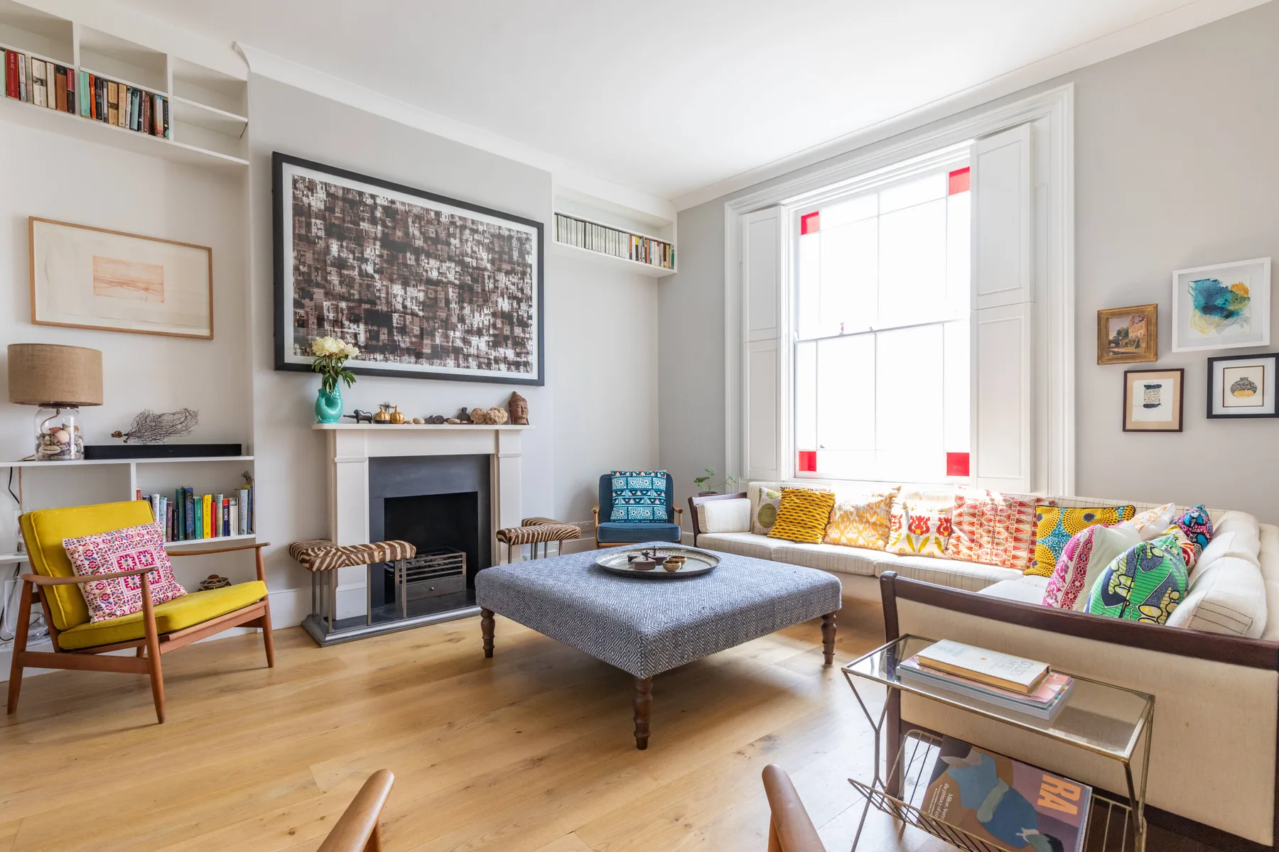 A bright living room with seating arranged around a central upholstered ottoman.