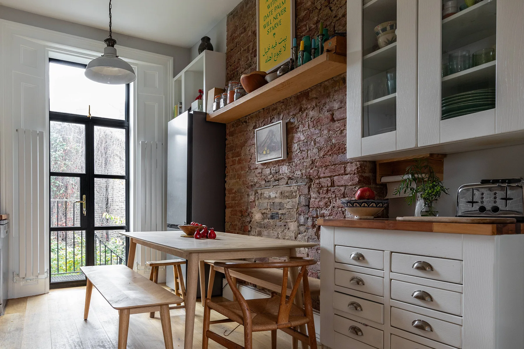 A kitchen and dining area with a wooden table beside exposed brick walls.