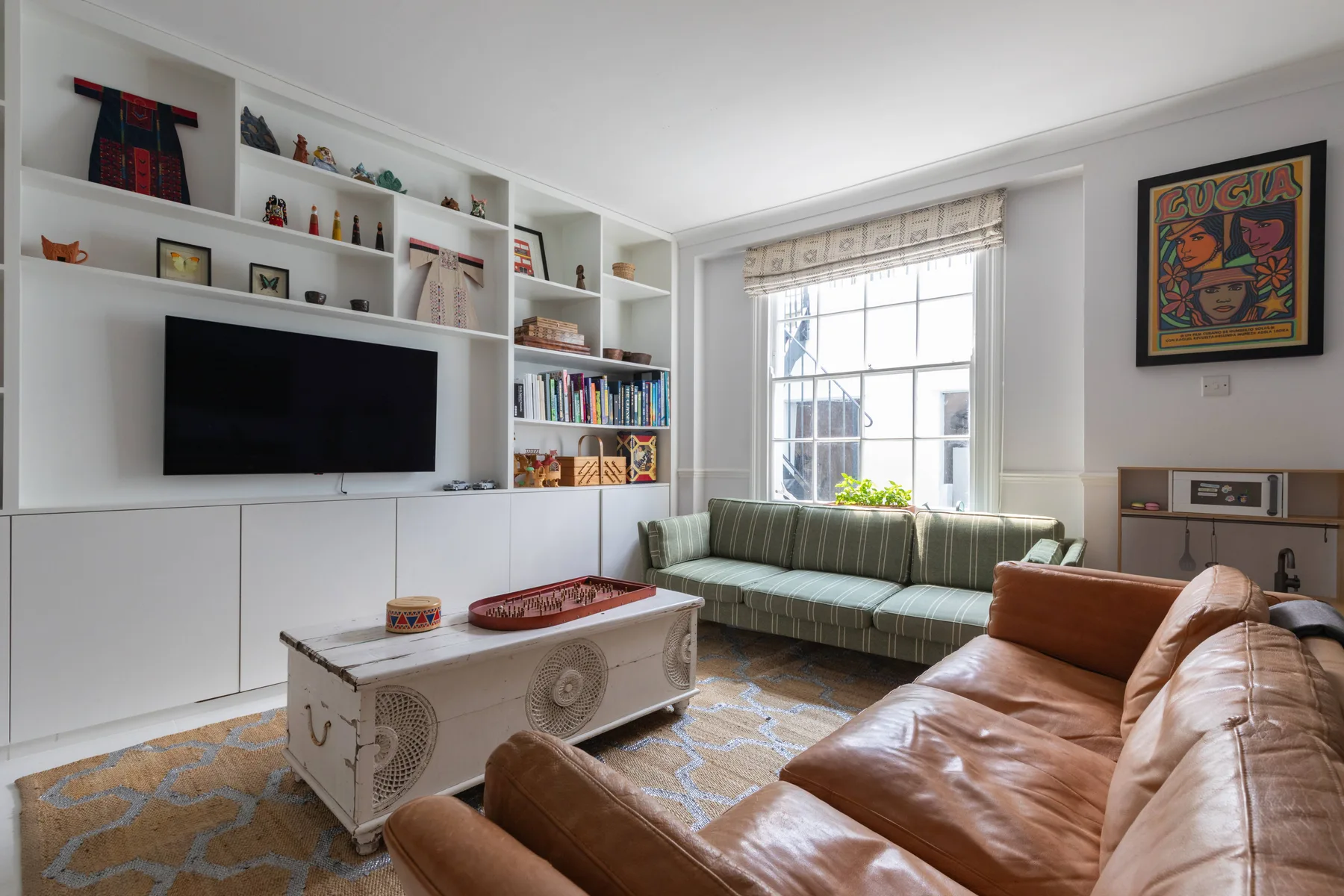 A bright living room with a television, built-in shelving, and seating by the window.