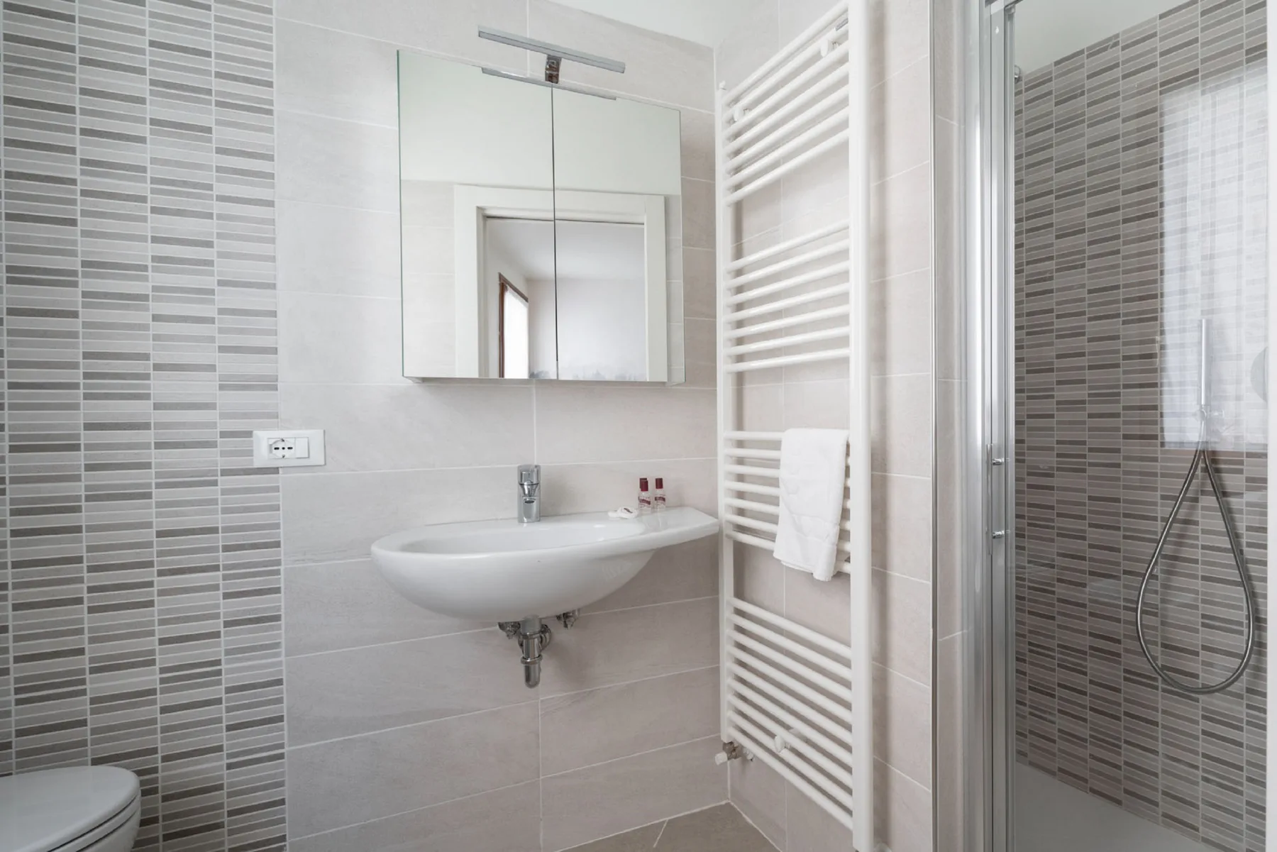 Un baño con azulejos, lavabo de pared, espejo y toallero calefactable.