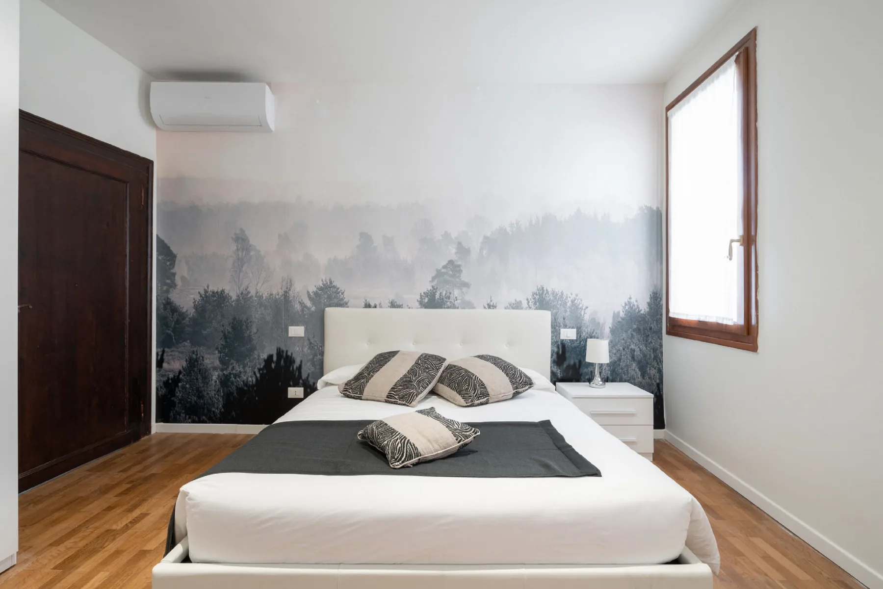 Un dormitorio con una cama doble, almohadas estampadas y un mural de bosque.