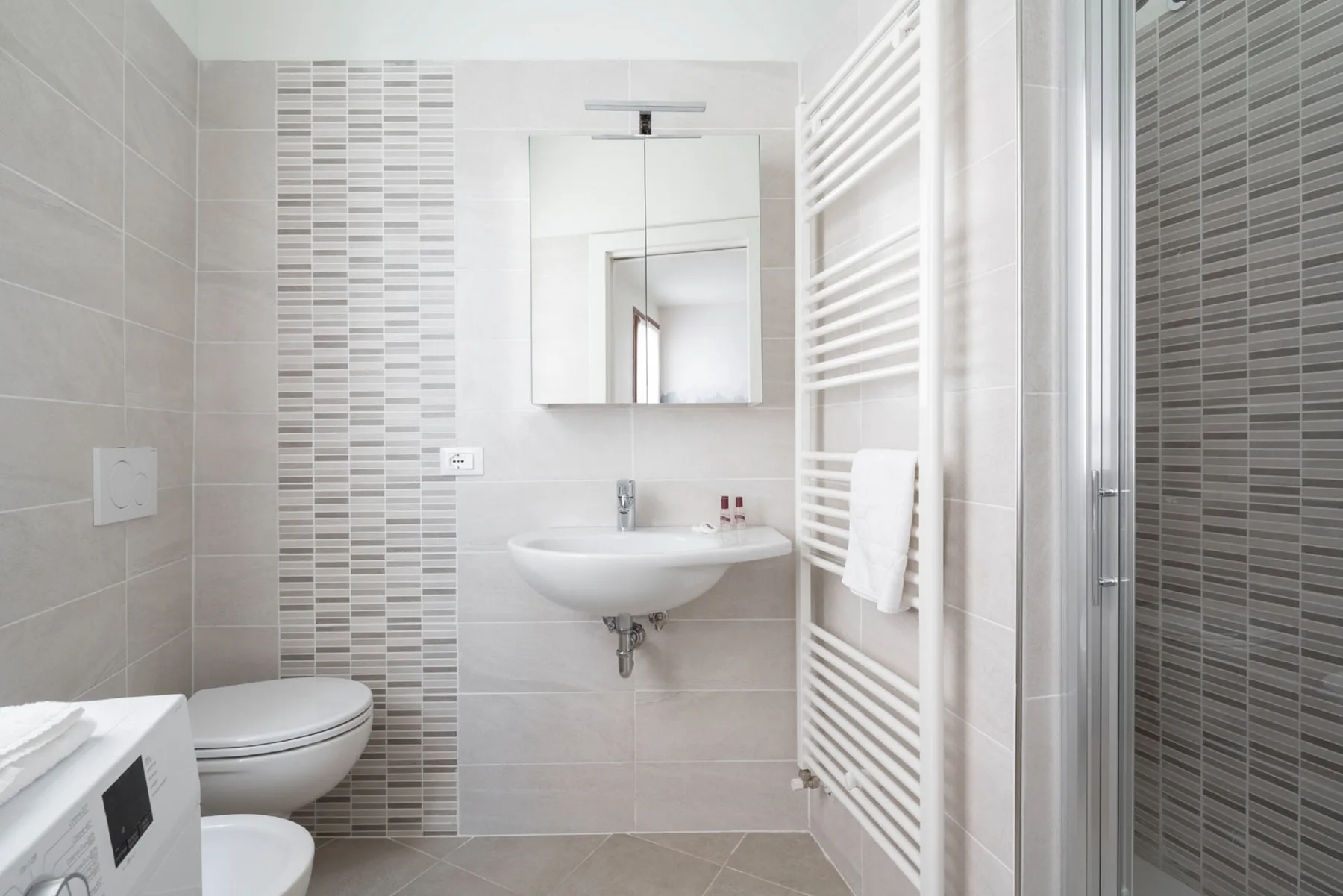 Un baño con azulejos, lavabo de pared y espejo.