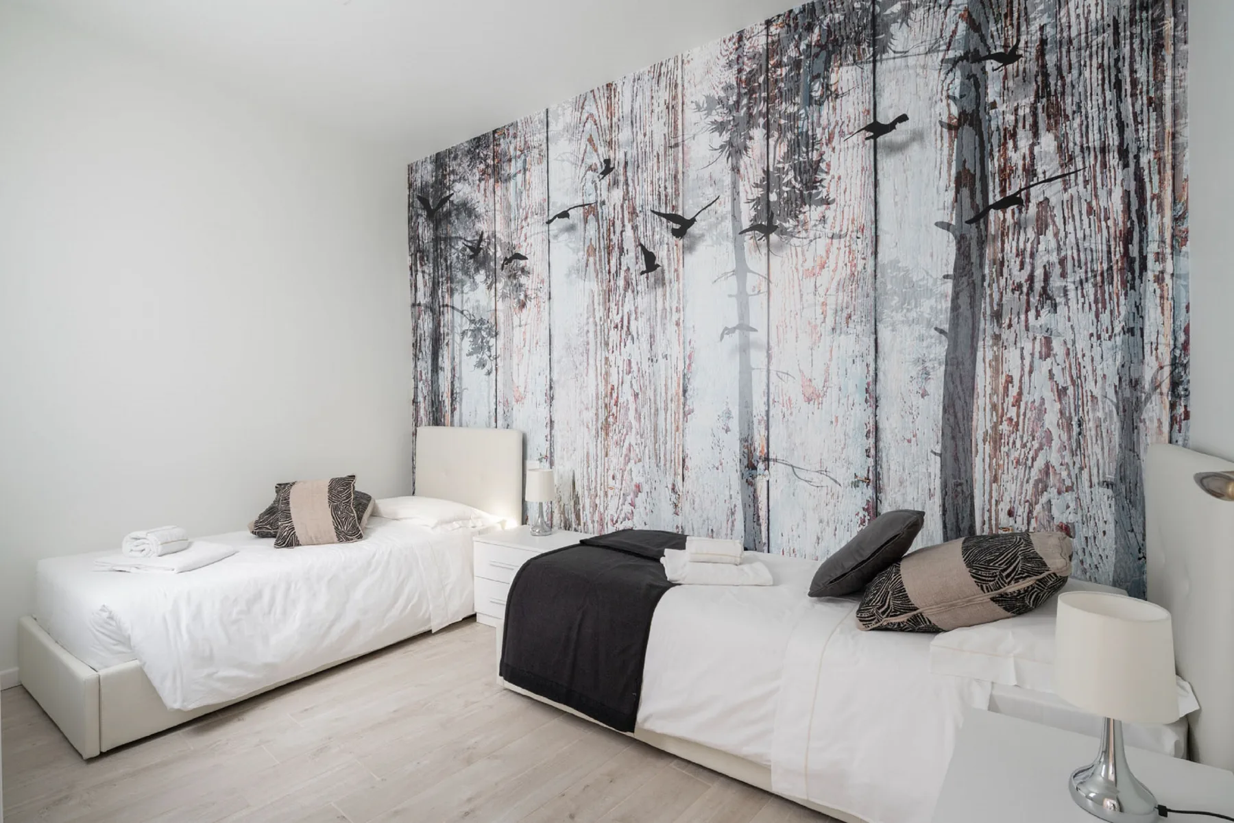 Un dormitorio luminoso con dos camas y un mural de bosque en la pared.
