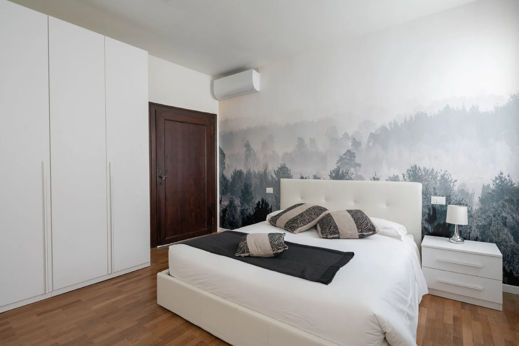 Un dormitorio con una cama blanca y un mural de bosque en la pared.