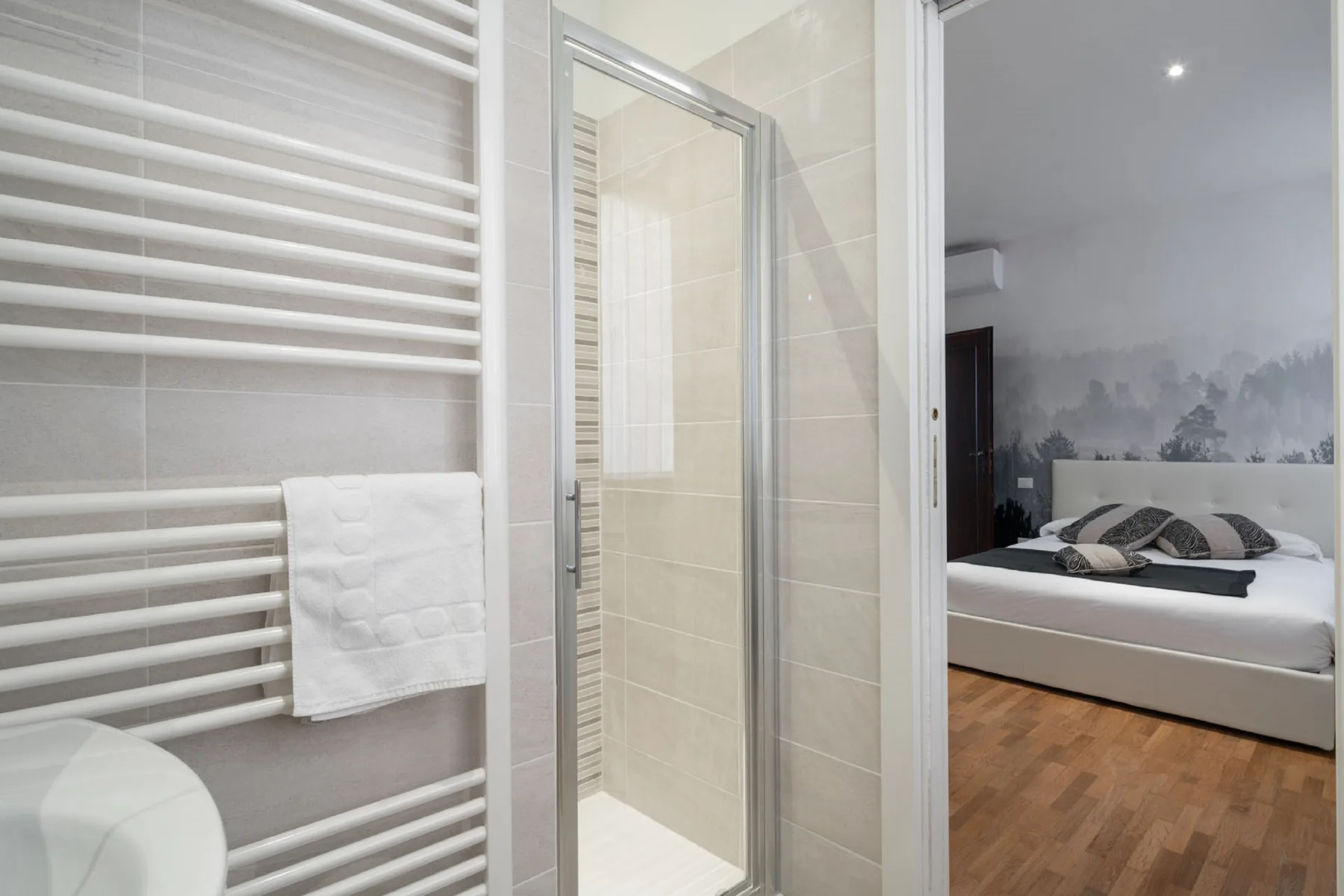 Un baño con ducha y toallero da a un dormitorio con una cama.