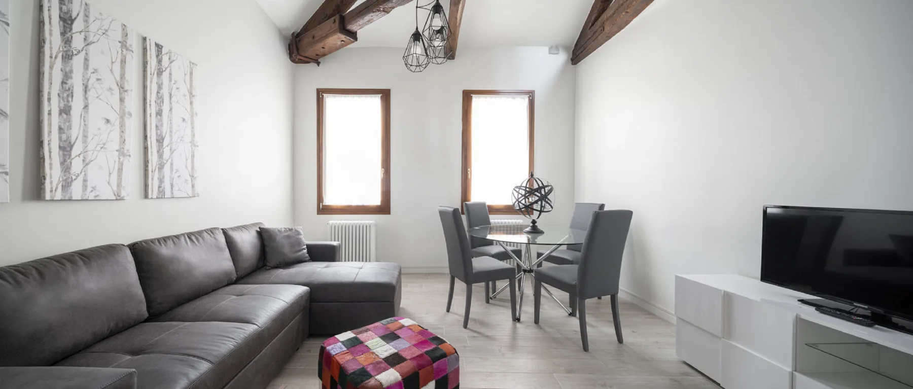 Una sala de estar con un sofá seccional gris, una mesa de comedor y un televisor.