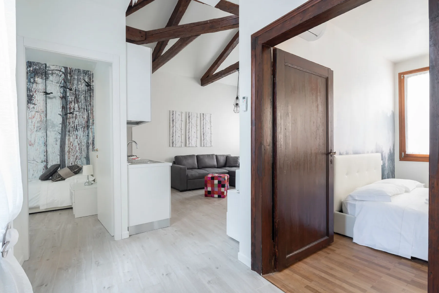 Un interior luminoso muestra una sala junto a un dormitorio con una puerta de madera abierta.