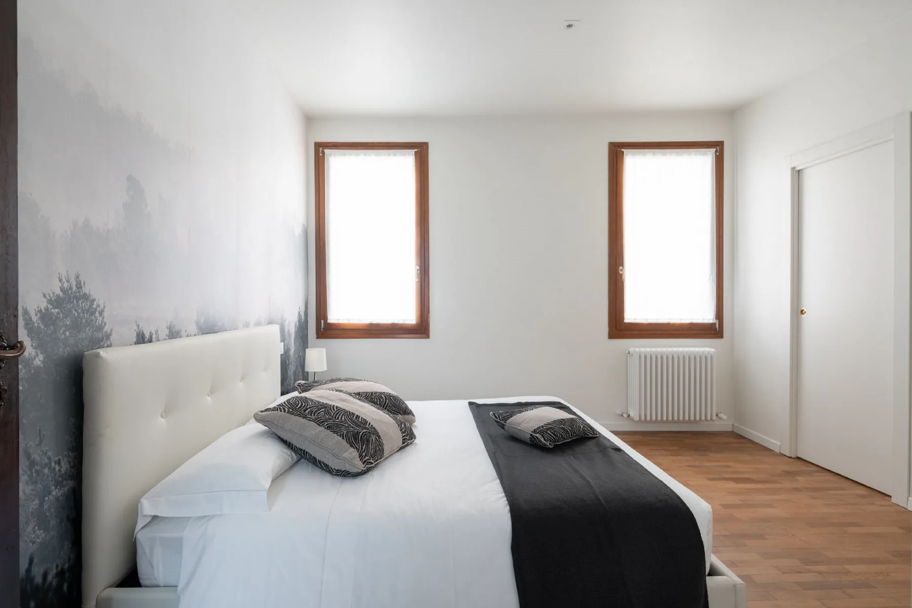 Un dormitorio con una cama, dos ventanas y un radiador.