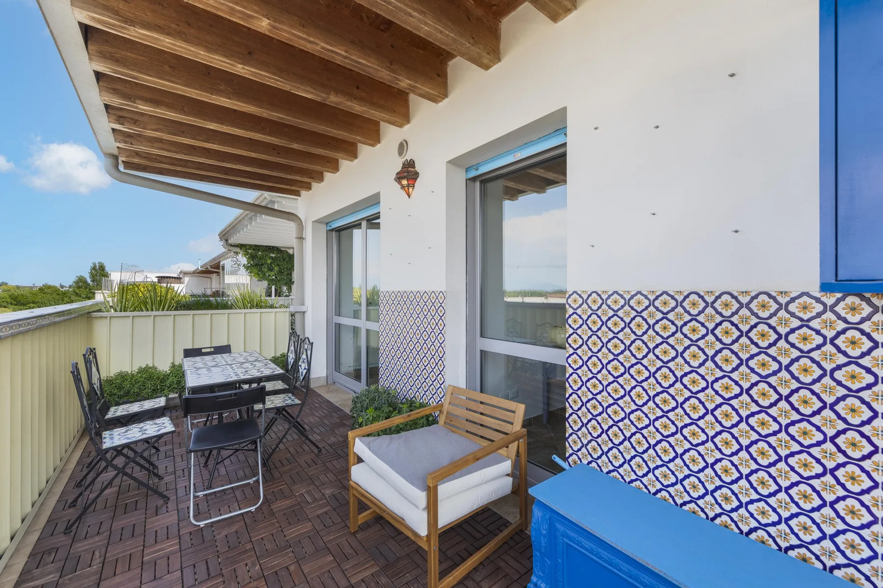 Una terraza amueblada con asientos, una mesa y azulejos estampados en la pared.