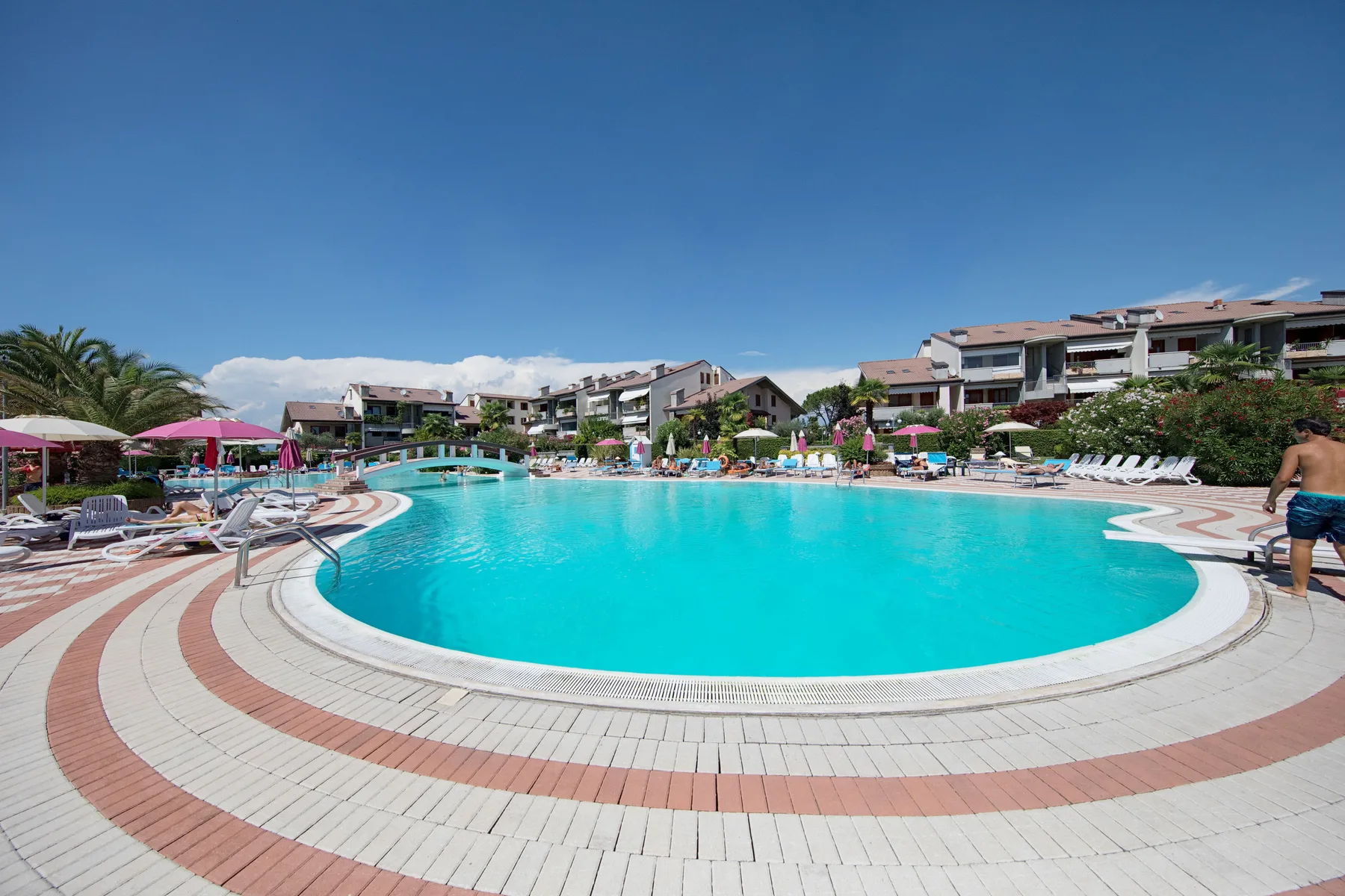 Una gran piscina al aire libre está rodeada de tumbonas y edificios de apartamentos.