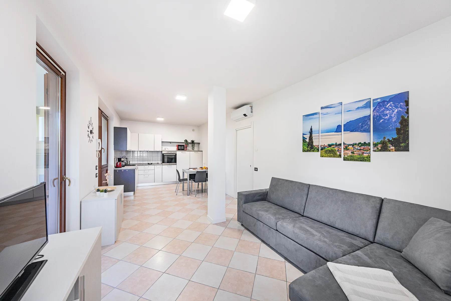 Una luminosa sala de estar abierta incluye asientos grises y una cocina al fondo.
