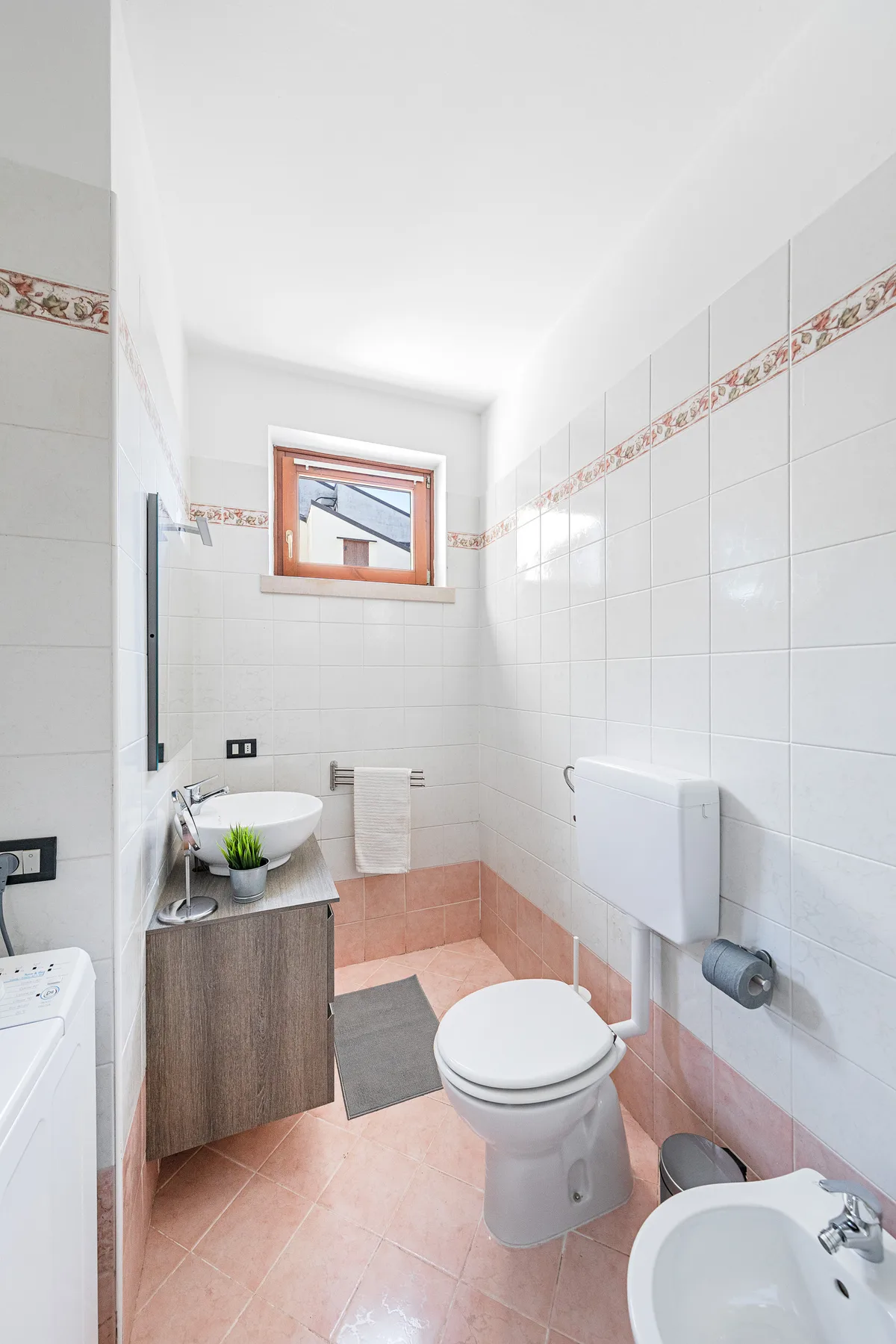 Un baño de azulejos con lavabo, inodoro y una ventana pequeña.