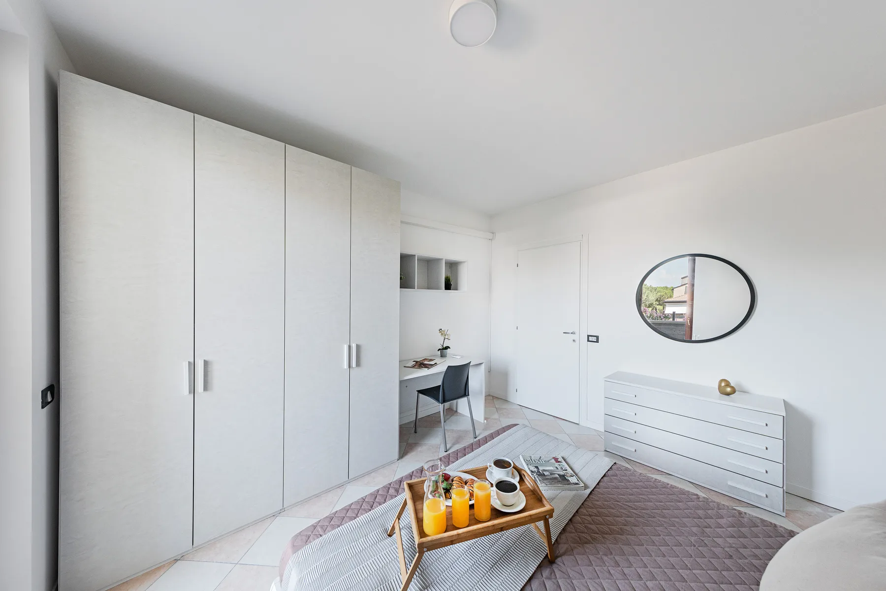 Un dormitorio luminoso con un armario grande, una cómoda baja y una pequeña zona de estar.