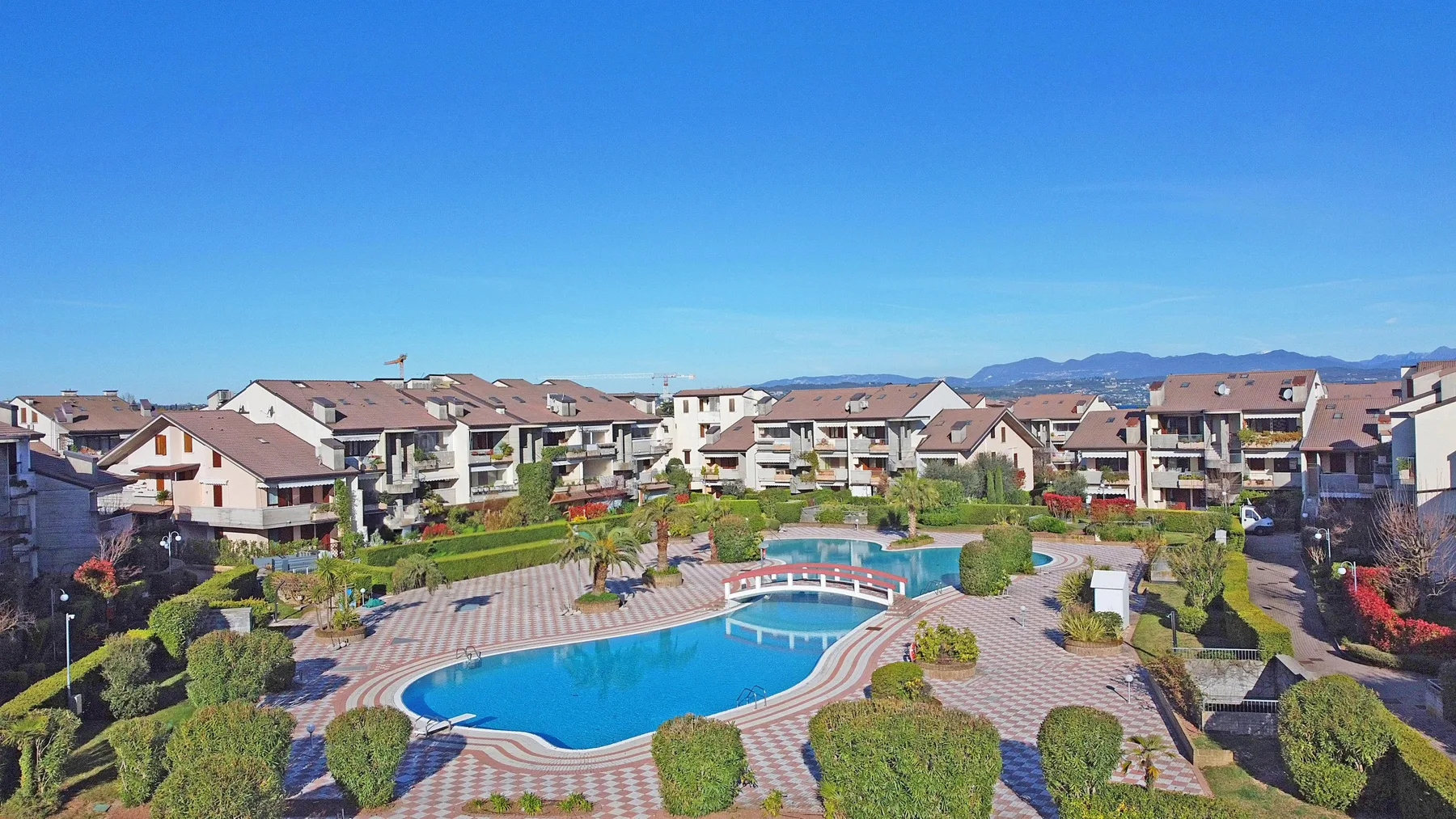 Un patio residencial ajardinado cuenta con una piscina y viviendas alrededor.