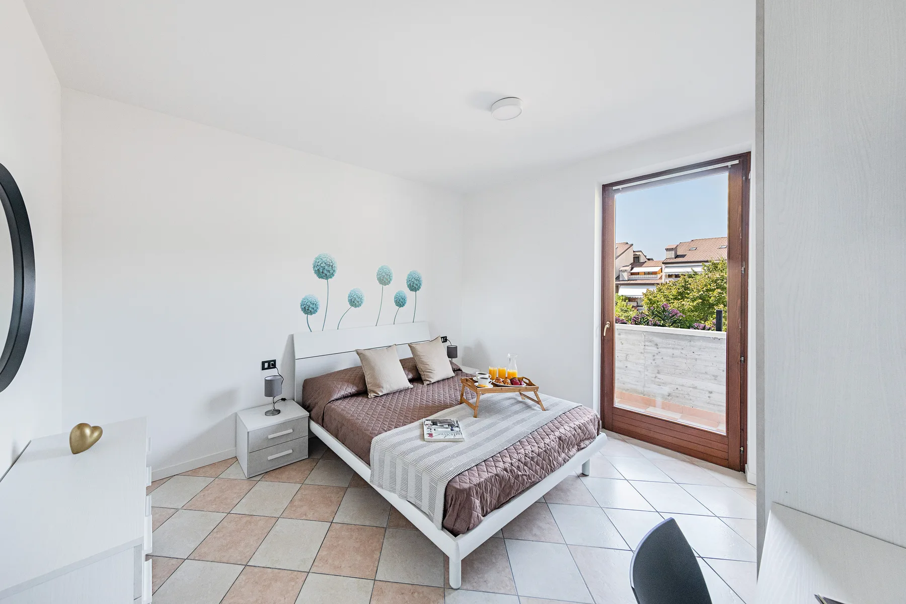 Un dormitorio luminoso con una cama junto a una puerta de vidrio que da a un balcón.