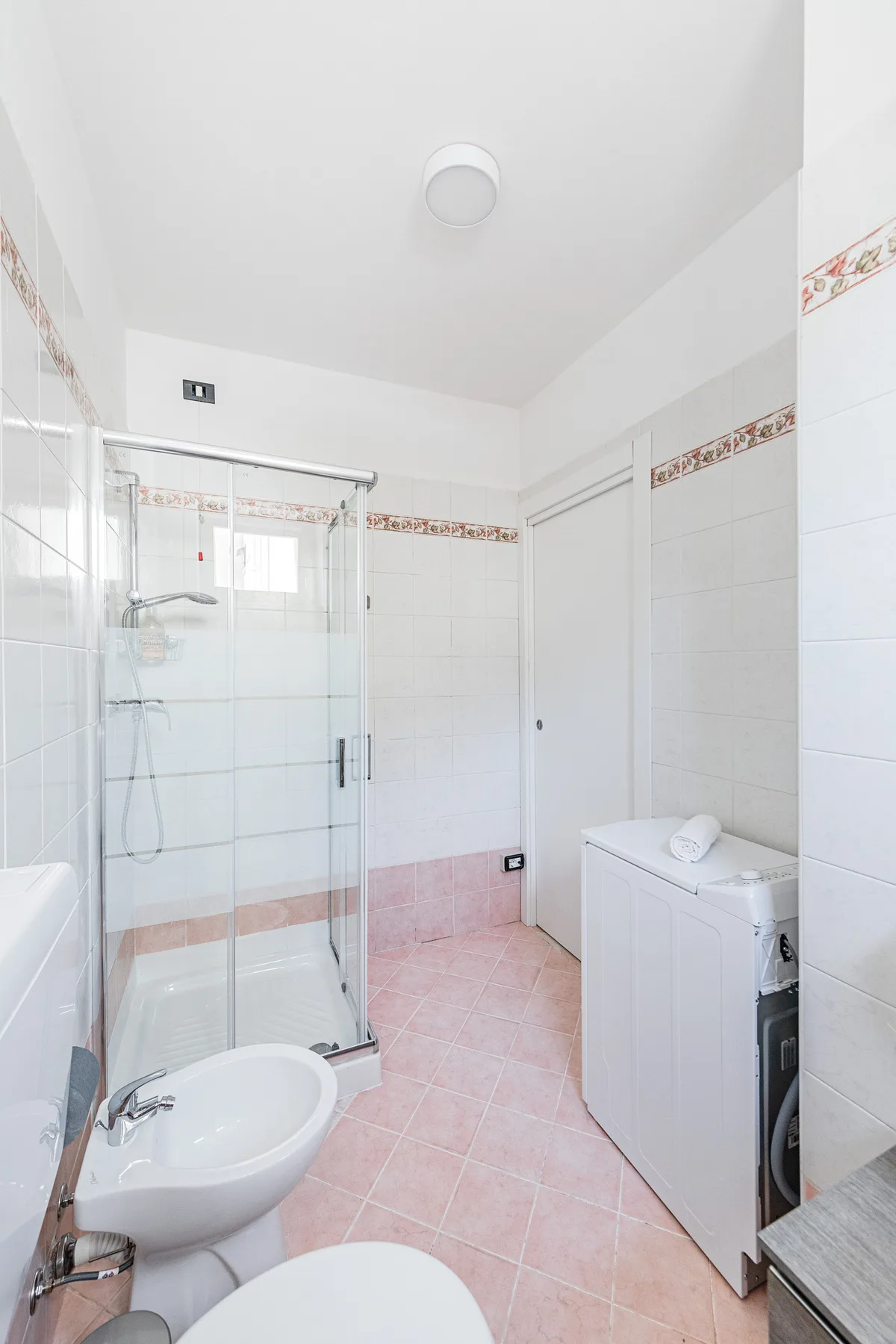 Un baño alicatado con ducha de cristal, lavabo y lavadora.