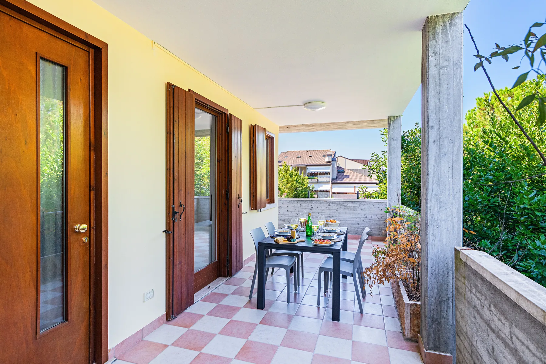 Un patio cubierto tiene una mesa de comedor y sillas junto a varias puertas de madera.