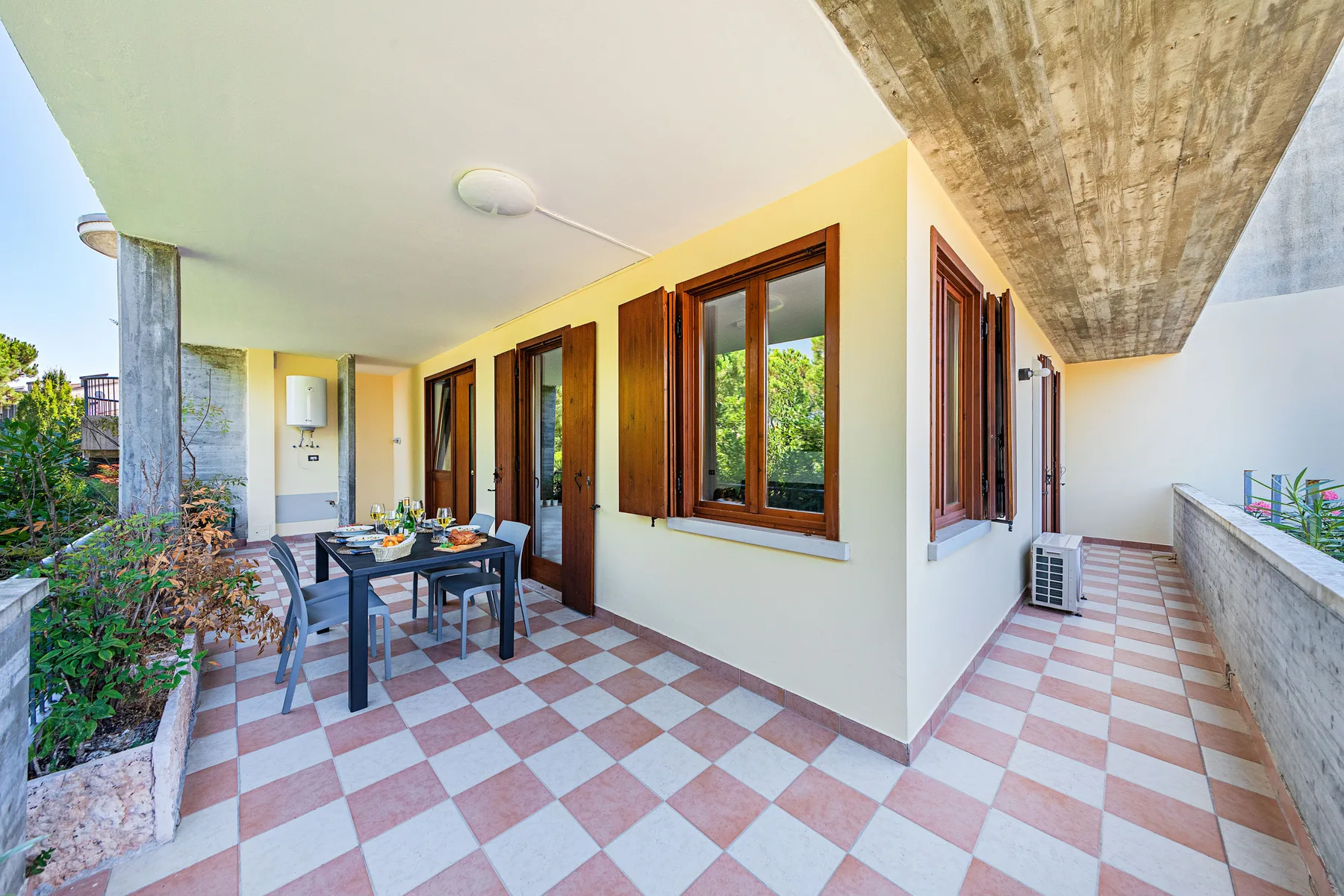 Una terraza cubierta con una mesa de comedor y ventanas junto a la pared.