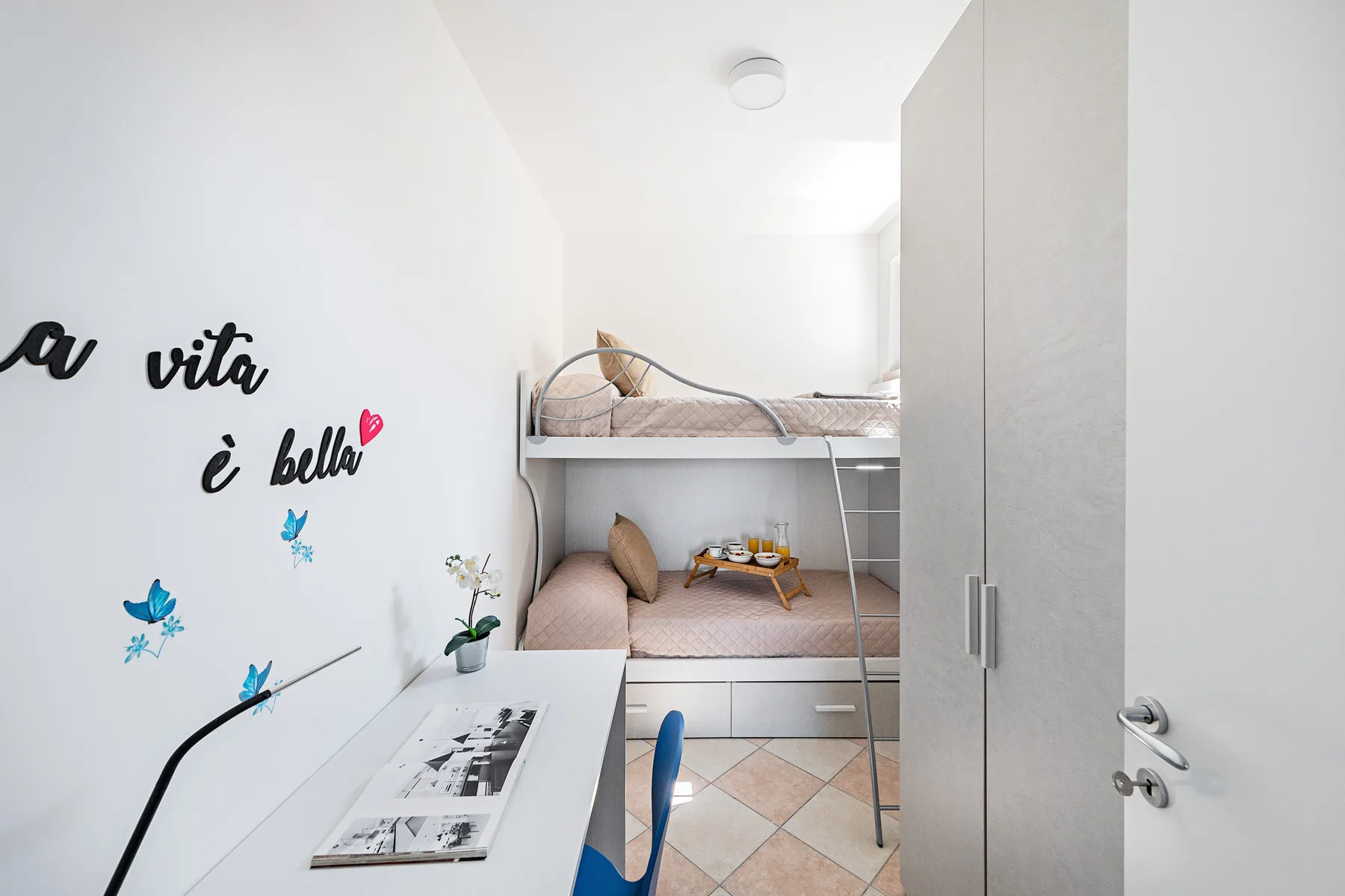Un dormitorio luminoso con literas, un escritorio y un armario alto.
