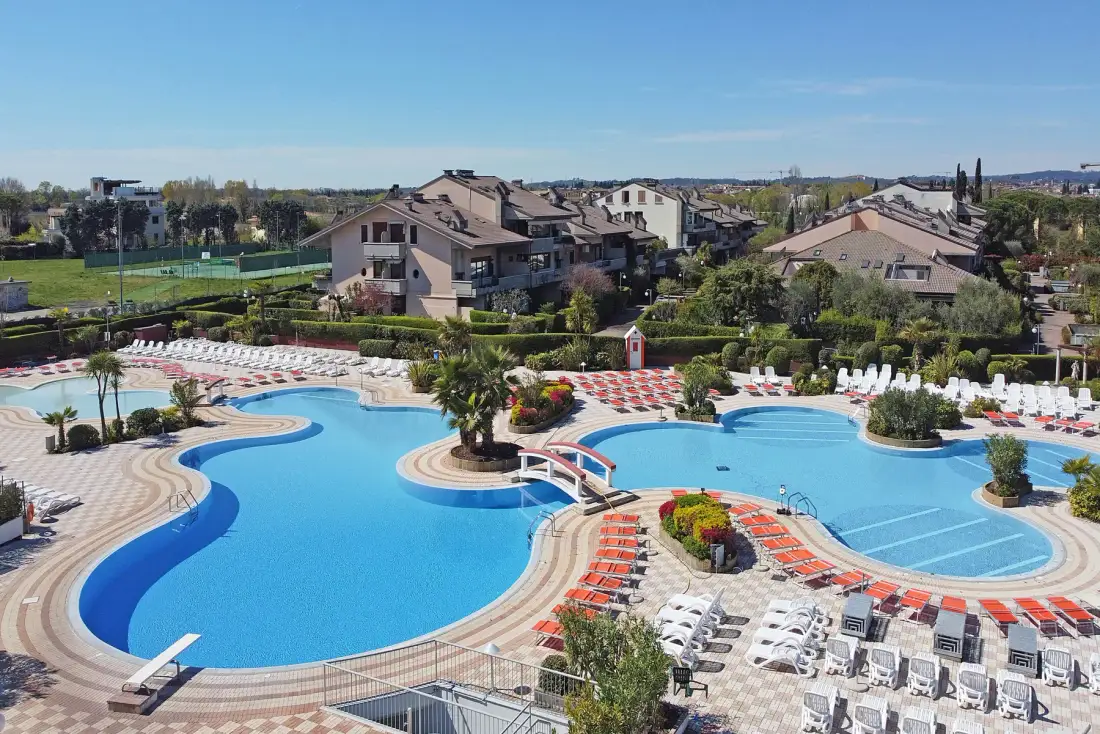Una piscina al aire libre con zonas de descanso y edificios residenciales cercanos.