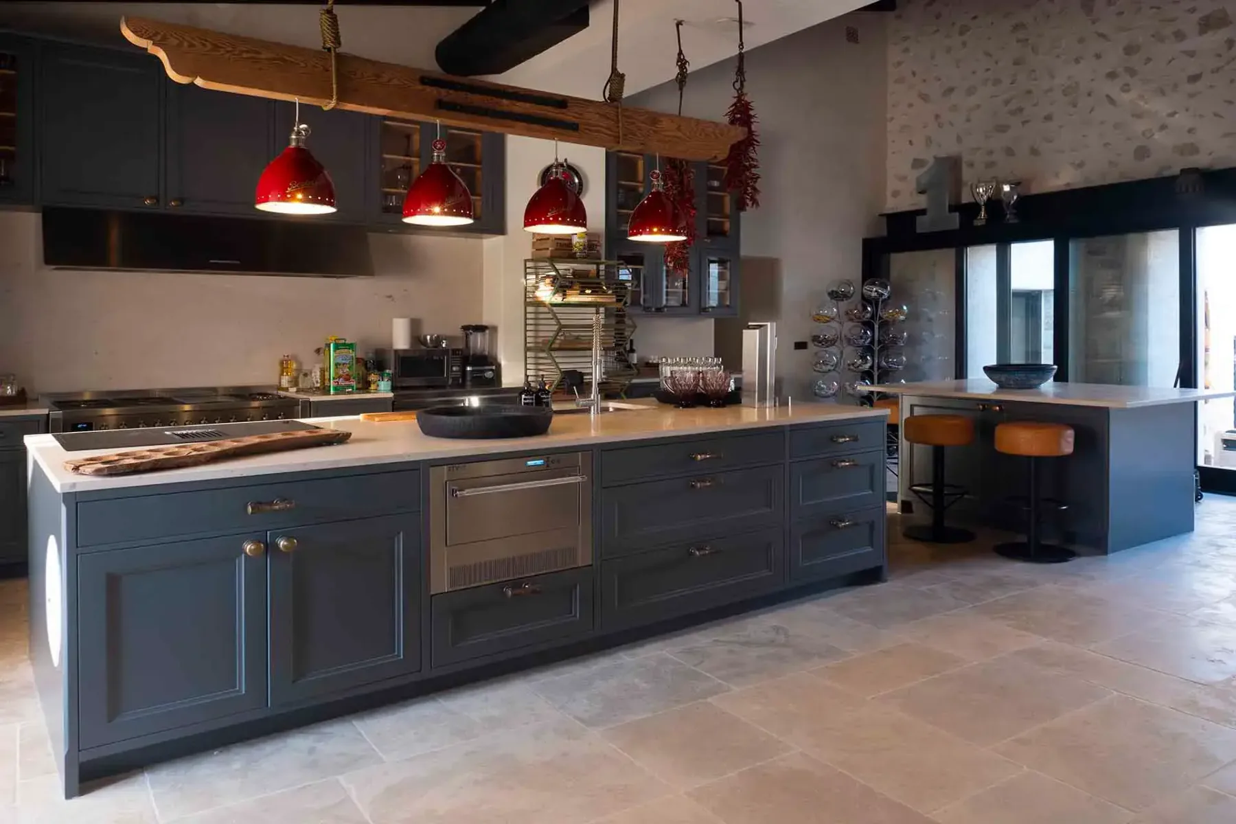 Spacious kitchen with dark cabinets, central island, stainless steel appliances, red pendant lights, and stone wall accents.