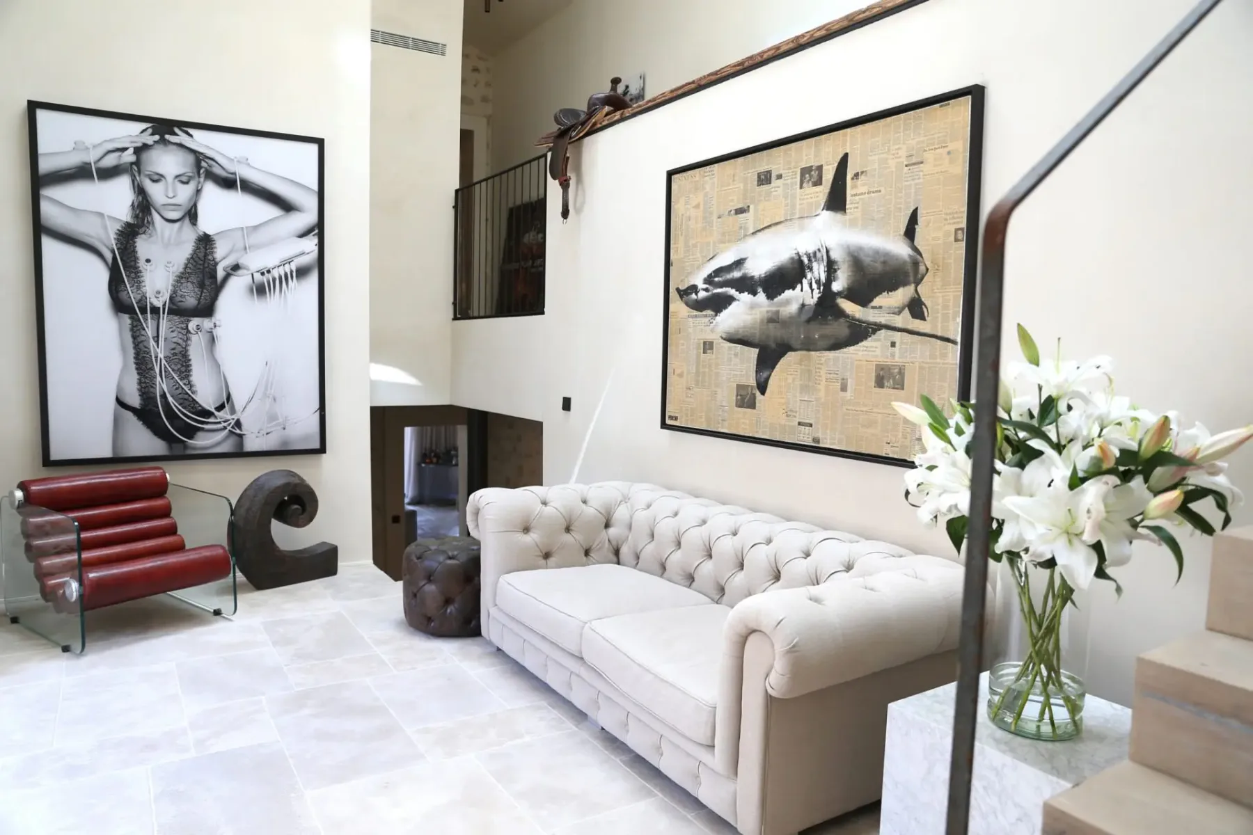 Stylish living room with a tufted sofa, large art pieces featuring a woman and a shark, a red chair, a large