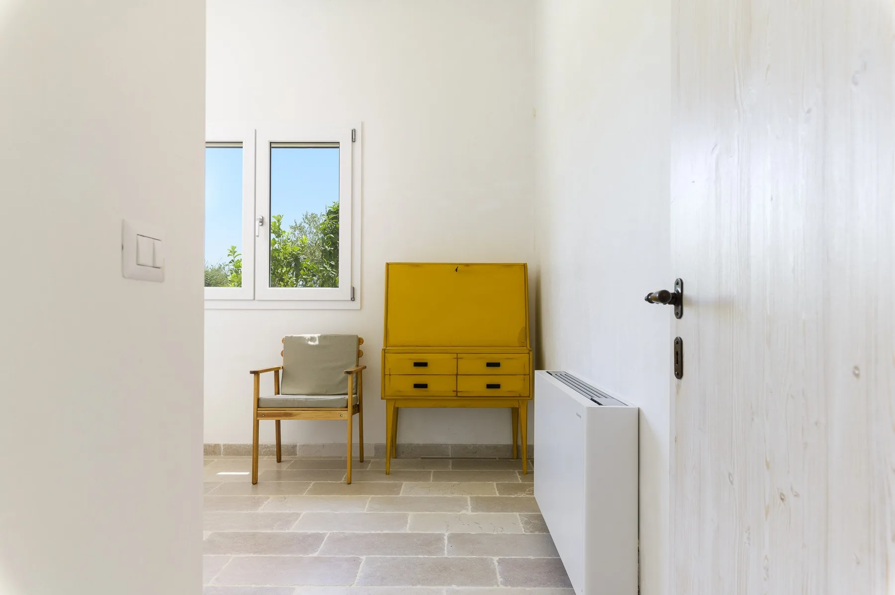 Una habitación luminosa con un mueble amarillo y una silla de madera junto a una ventana.