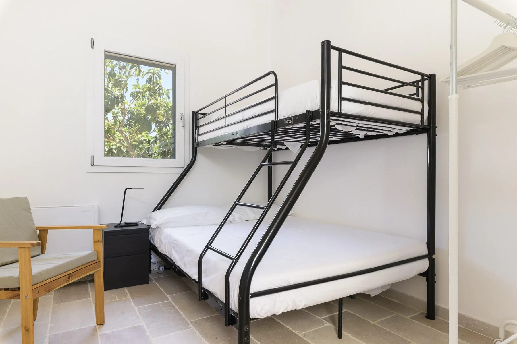 Un dormitorio con una litera negra y una ventana con vista a la vegetación.