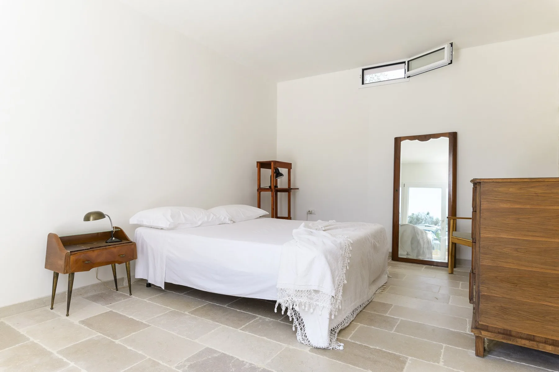 Un dormitorio luminoso con una cama, un espejo y muebles de madera.